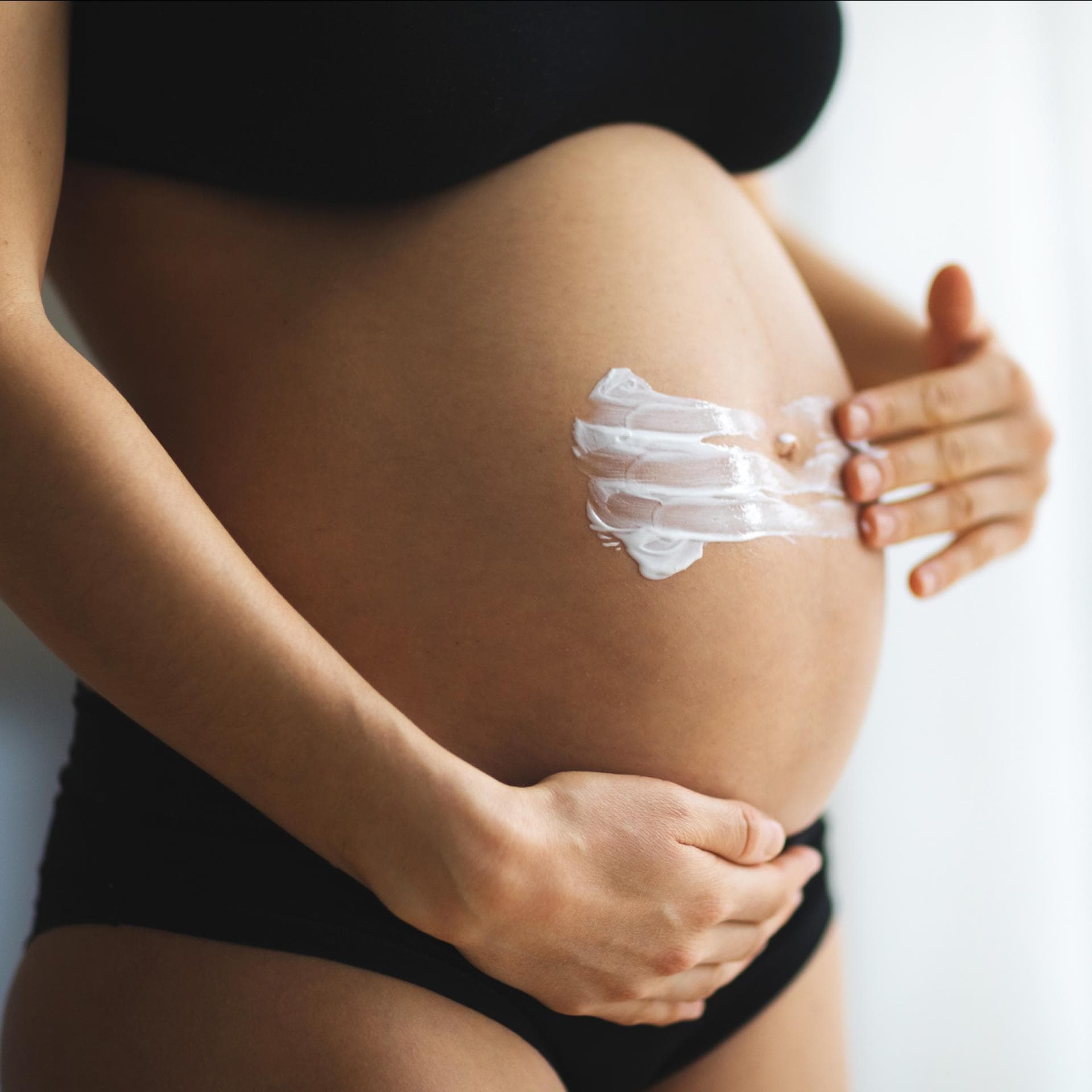 Eine Frau cremt ihren Babybauch ein.