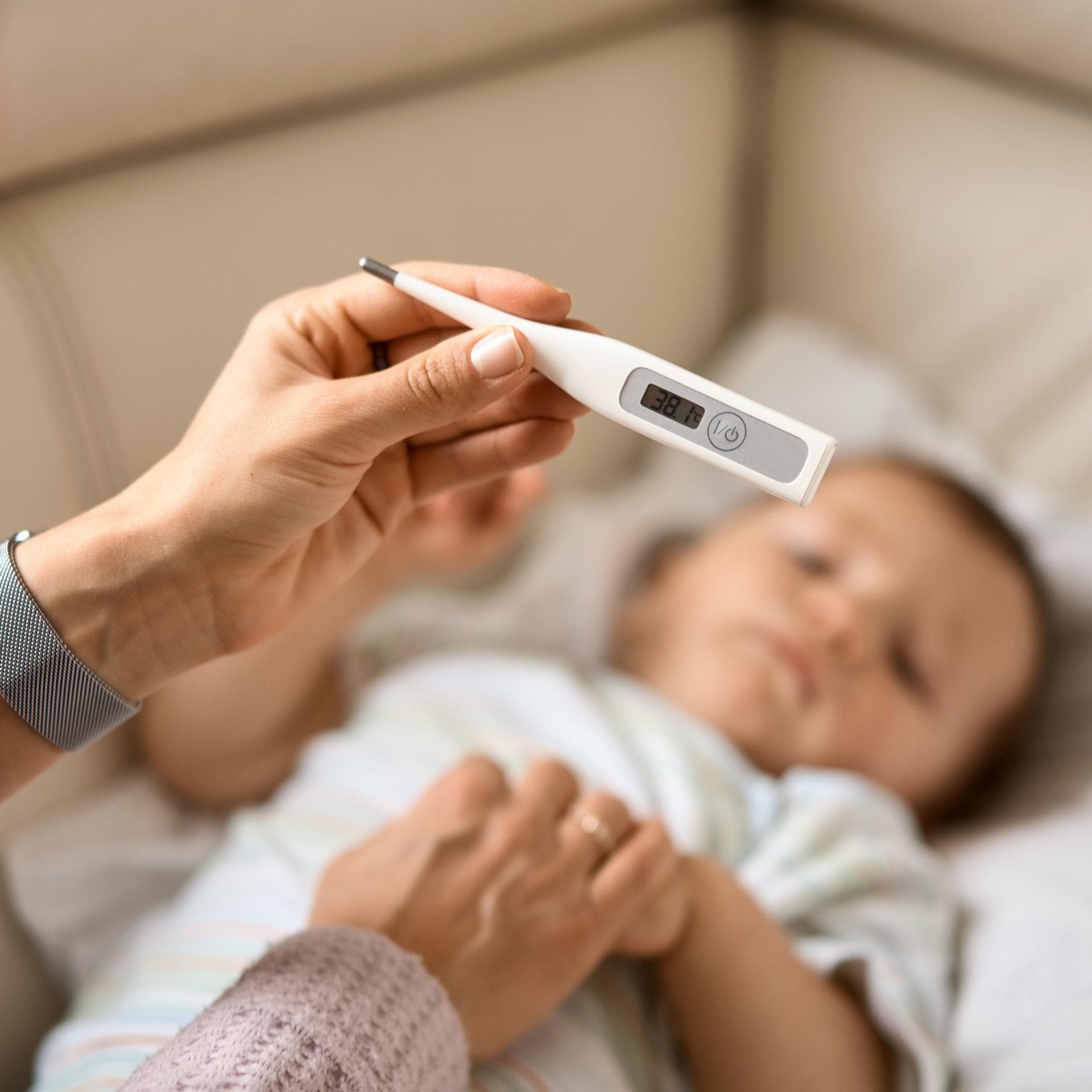 Eine Mutter hält das Fieberthermometer über ihrem Baby.