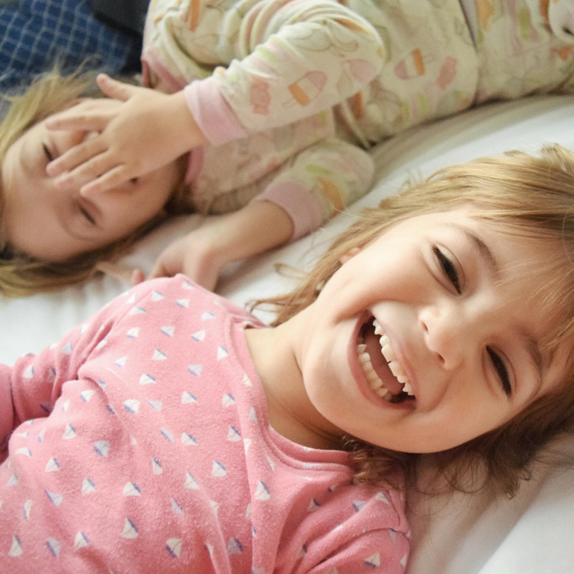 Zwei Kinder liegen lachend im Bett