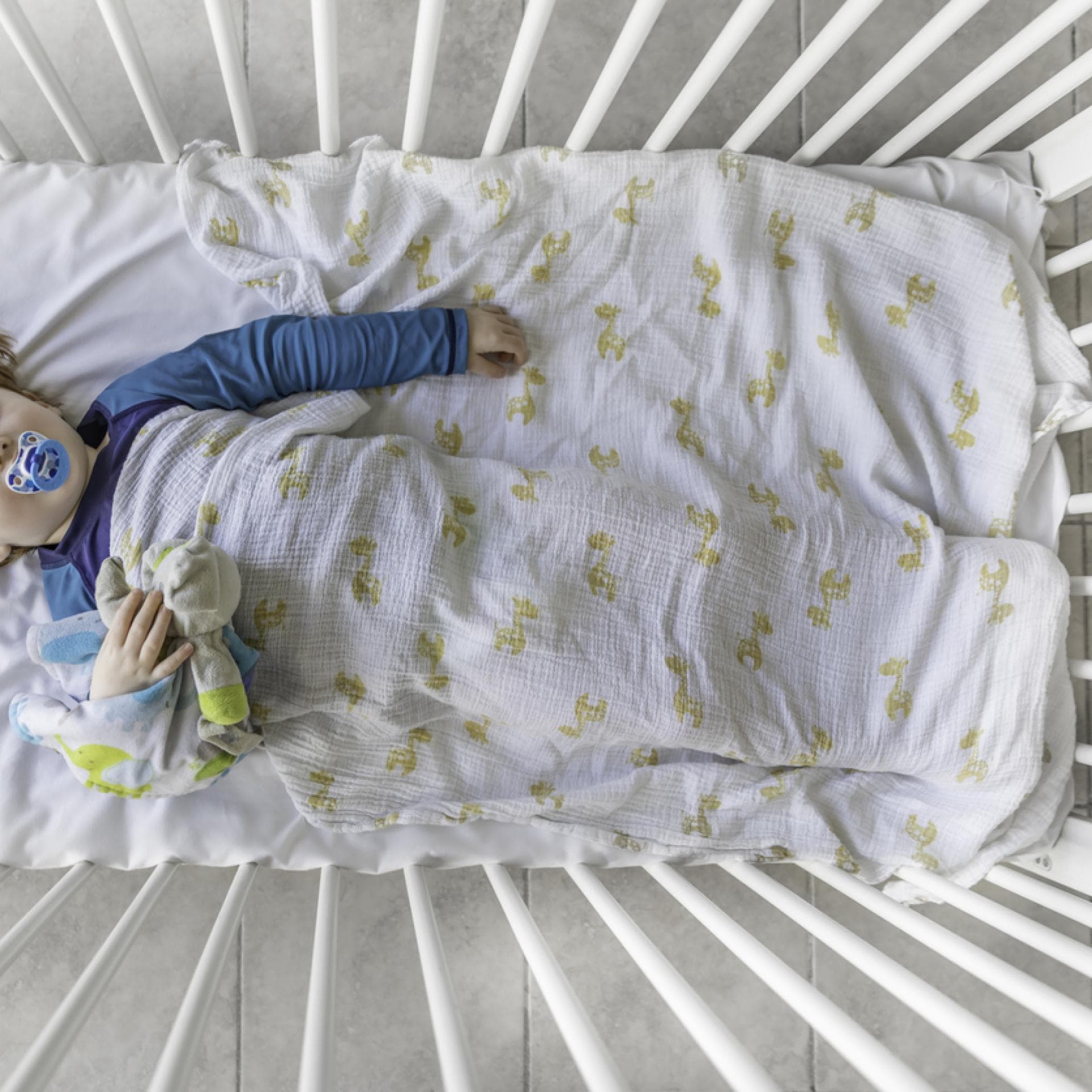 Rothaariges Kleinkind mit Schnuller liegt schlafend im Gitterbett