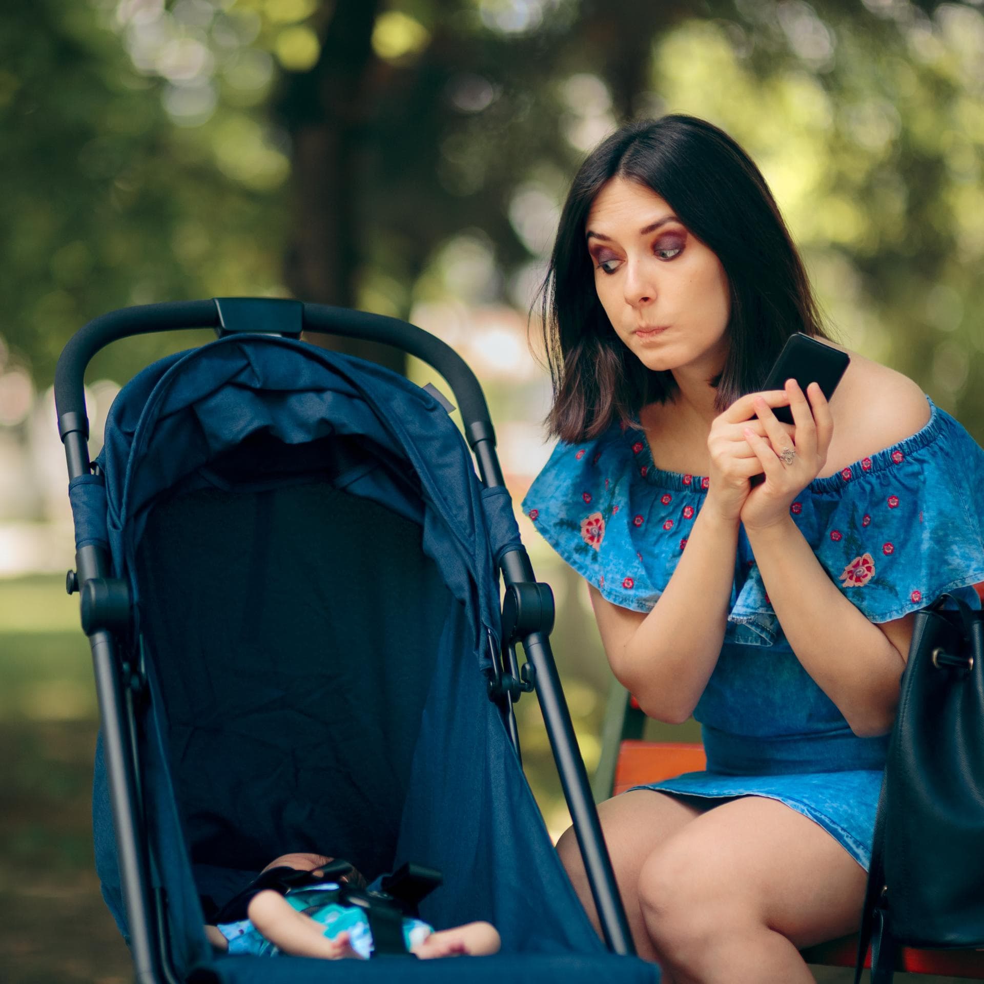 Frau sitzt mit Handy in der Hand neben dem Kinderwagen