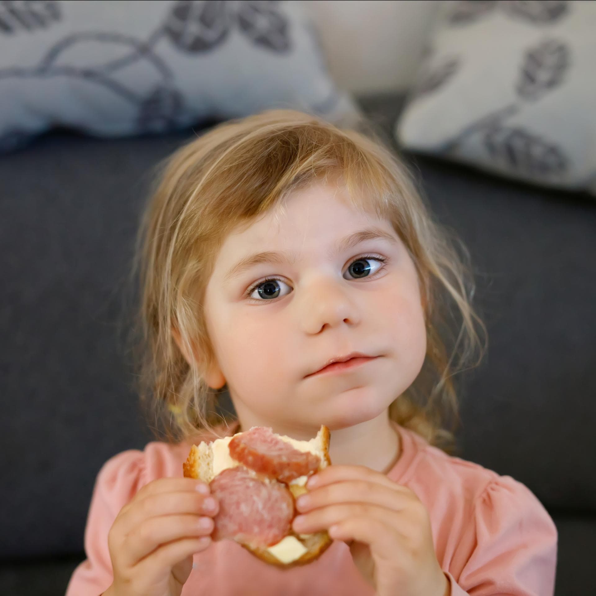 Kleines Mädchen isst Brot mit Salami.