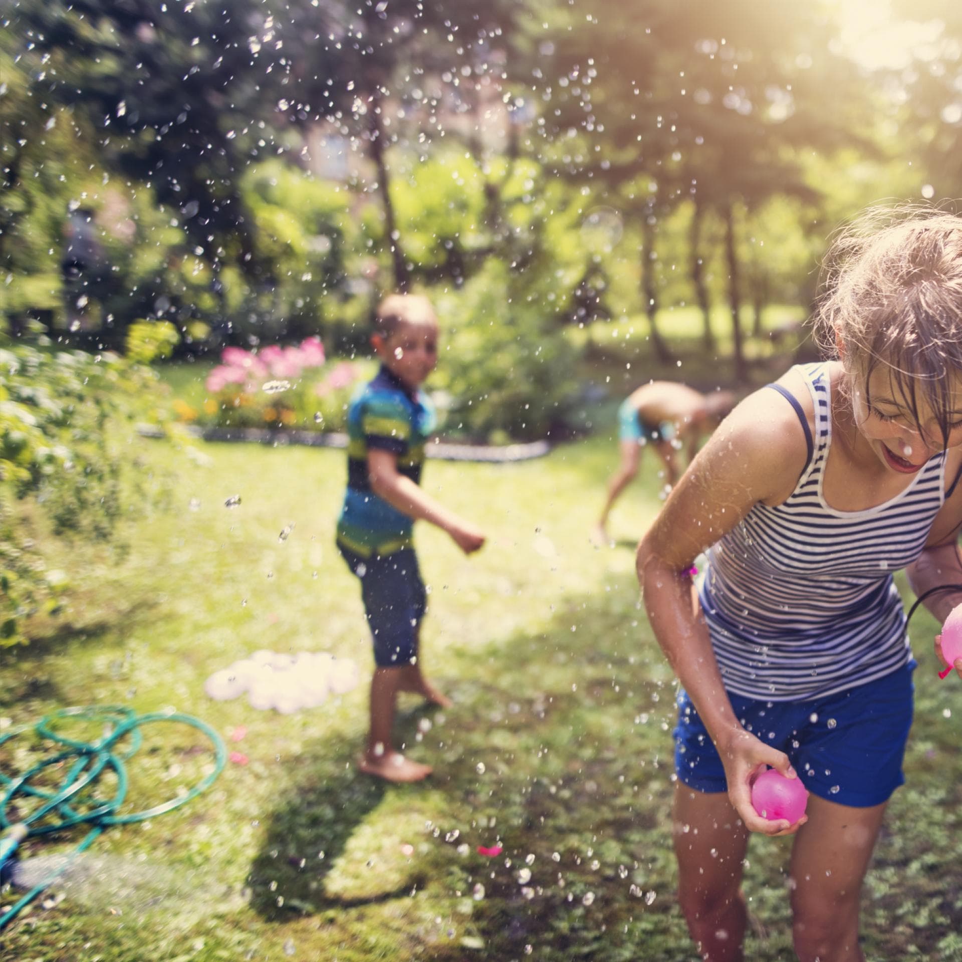 Zwei Kinder bewerfen sich im Garten mit Wasserbomben.