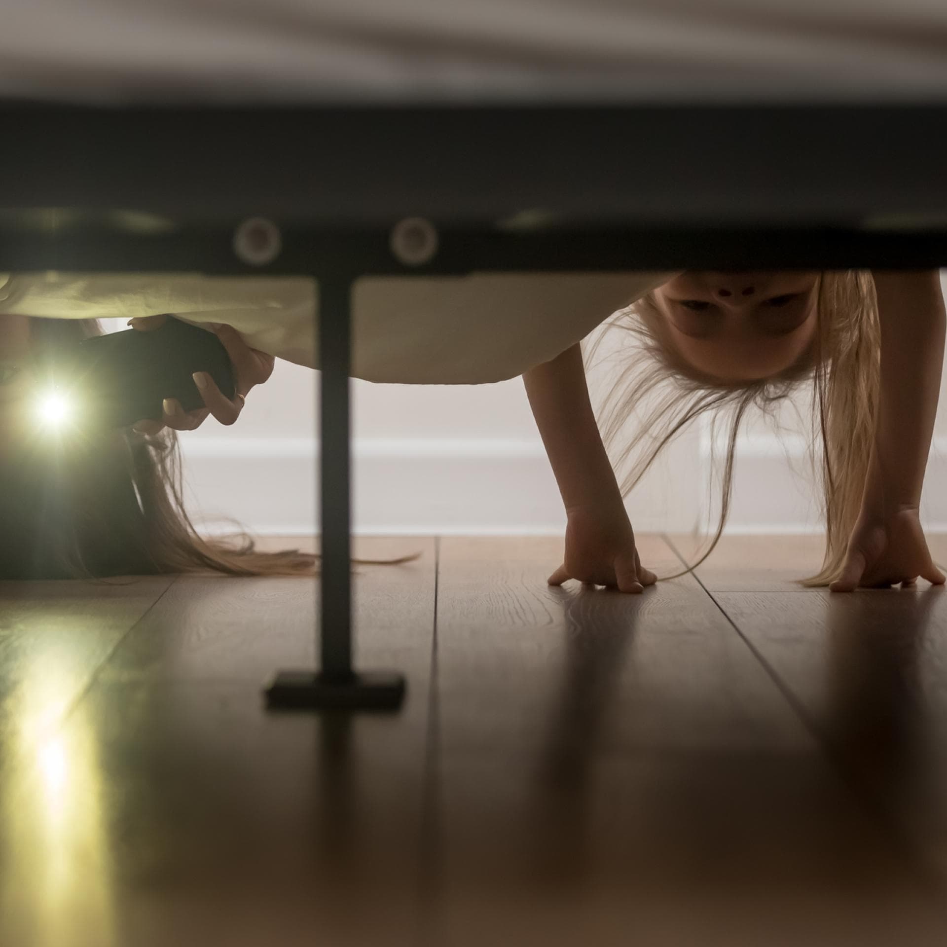 Mutter und Tochter schauen mit Taschenlampe unters Bett