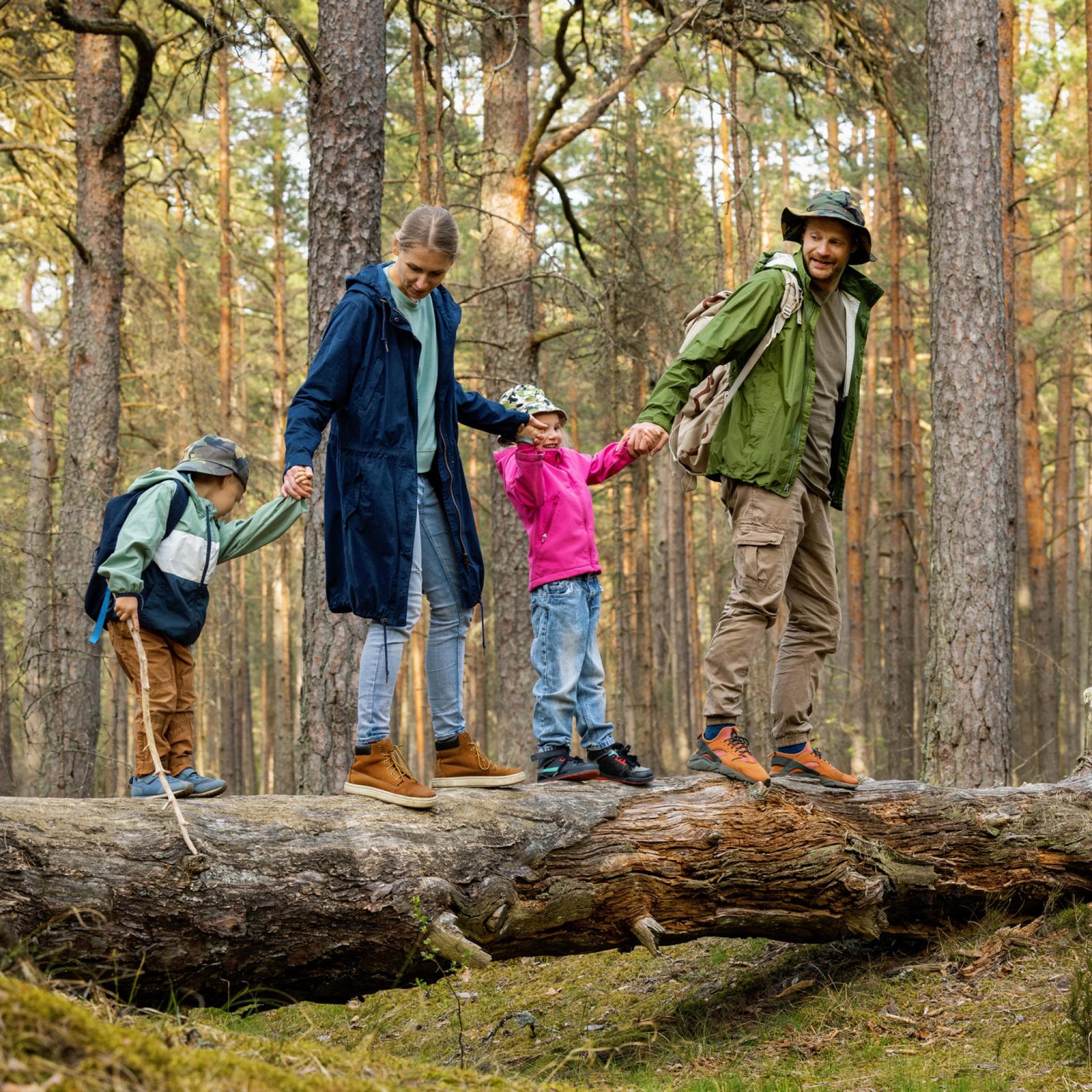 Familie läuft auf Baumstamm im Wald.