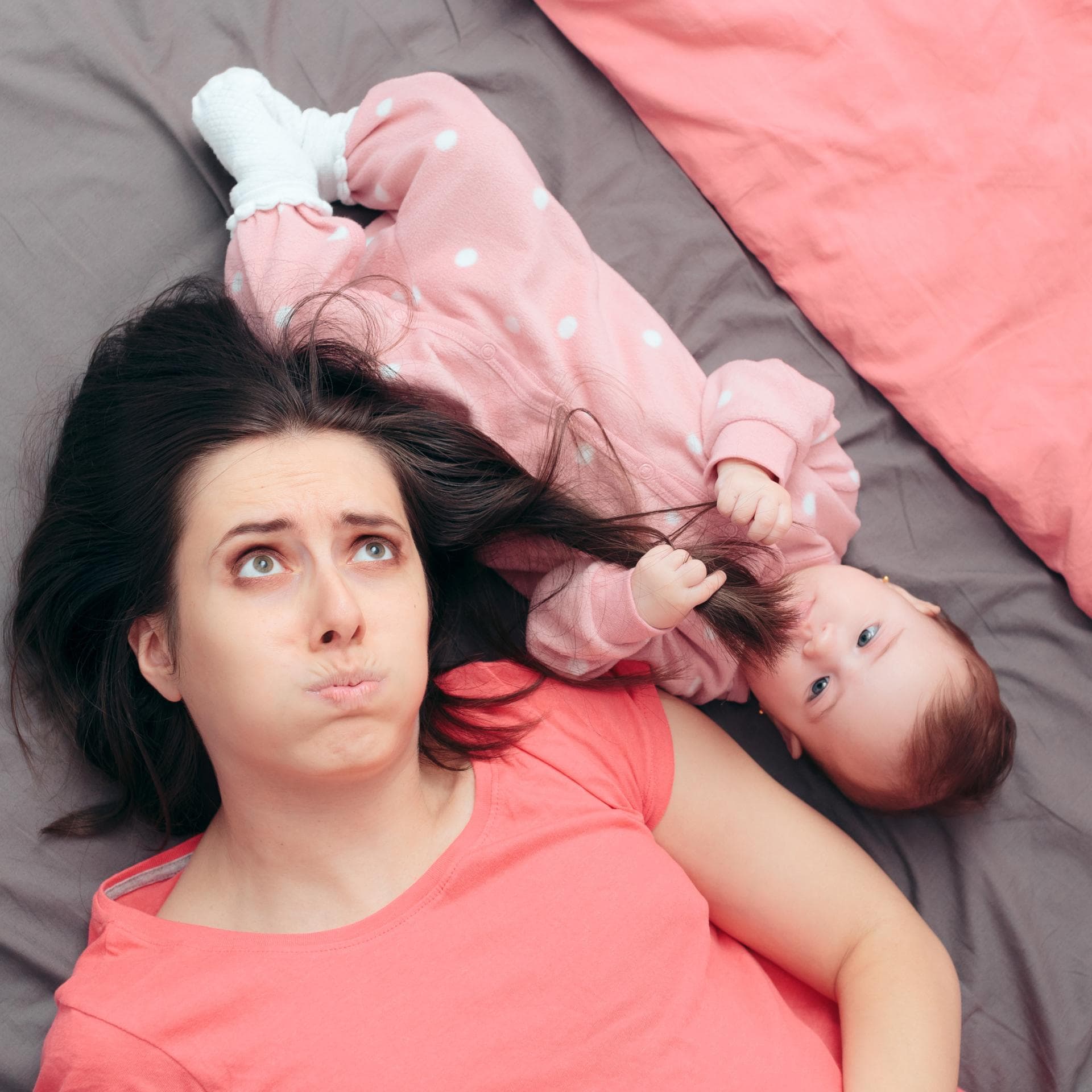 Mama liegt neben Baby auf dem Bett.
