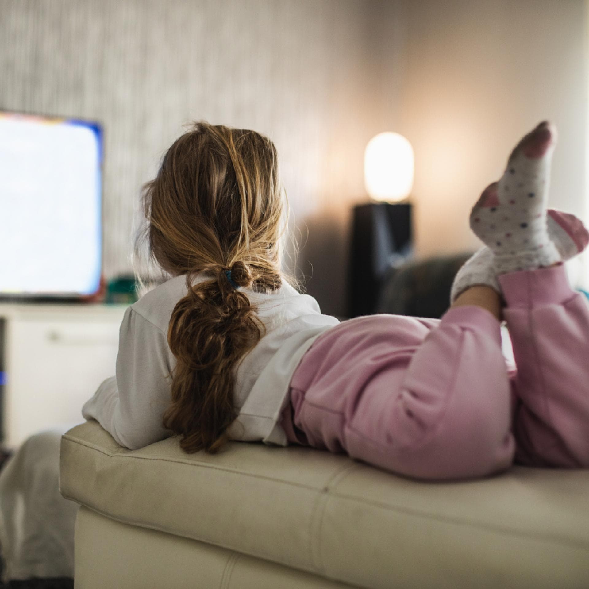 Ein Mädchen liegt auf dem Sofa und schaut eine Kinderserie.