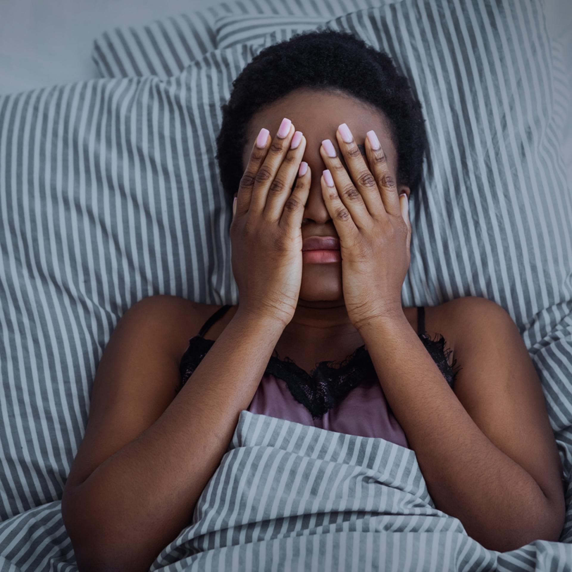 Eine Frau liegt mit Händen vor den Augen im Bett und kann nicht schlafen!