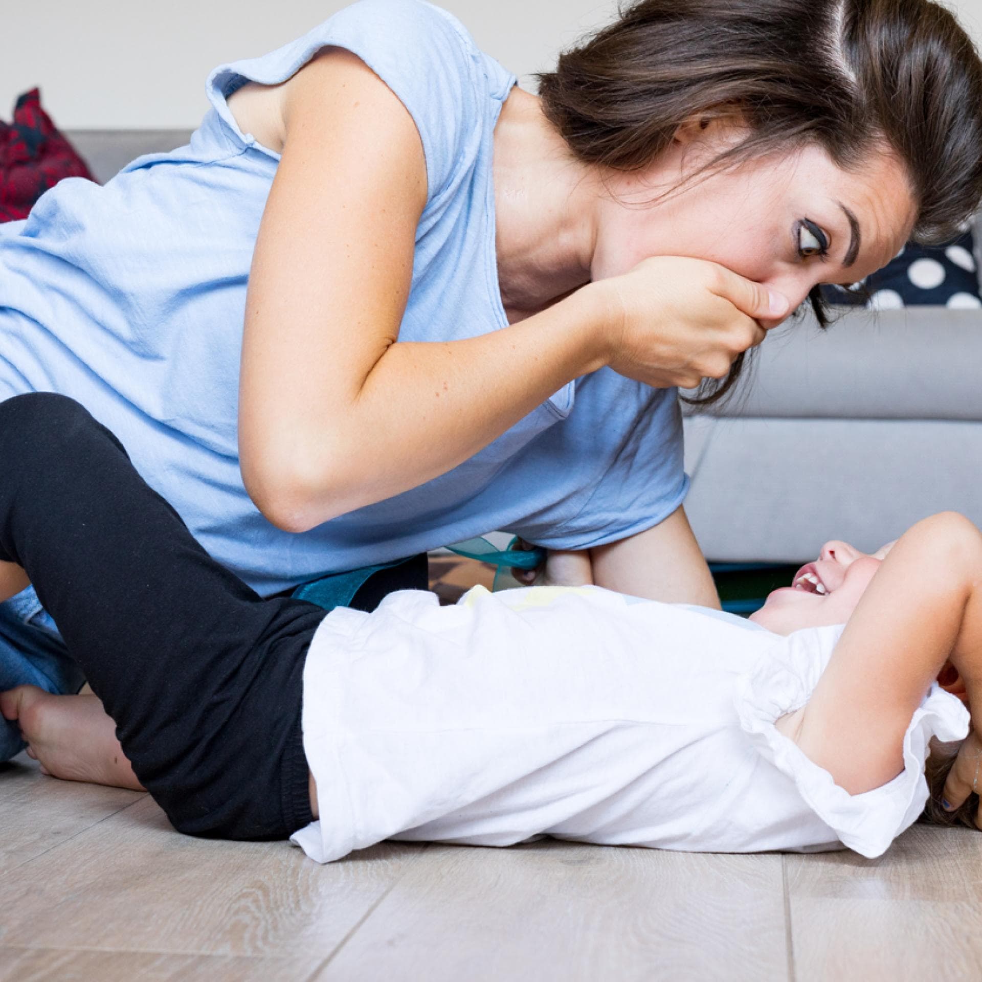 Eine Mutter spielt mit ihrer Tochter und hält sich die Hand vor den Mund.
