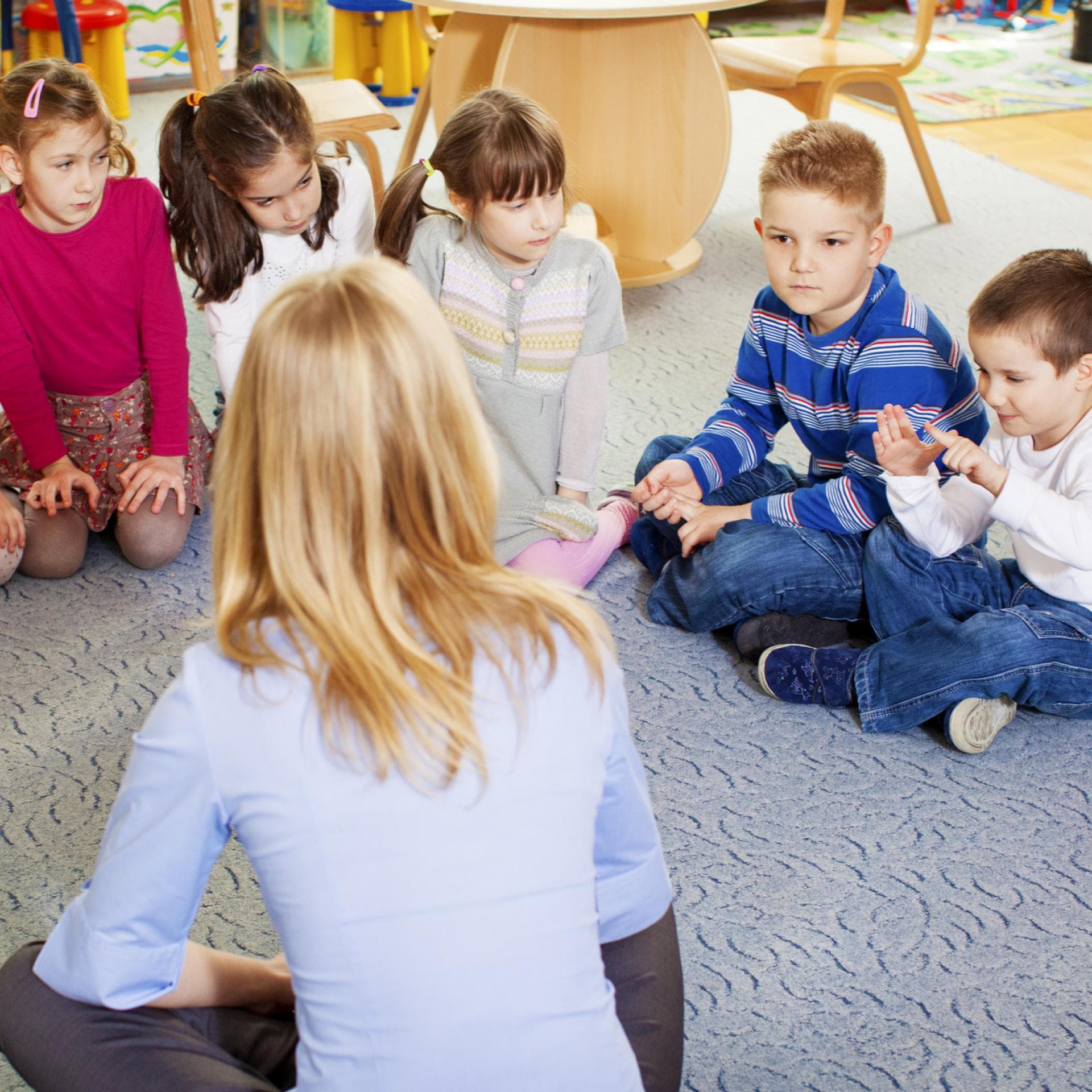 Kinder und Erzieherin sitzen im Kreis.