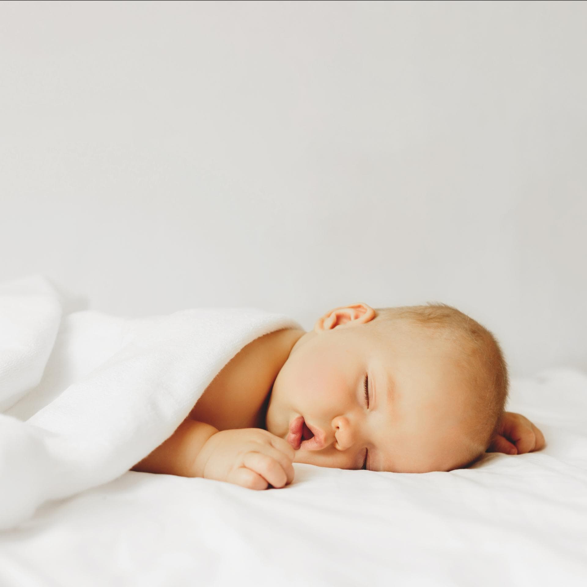 Baby schläft zugedeckt auf dem Bett.