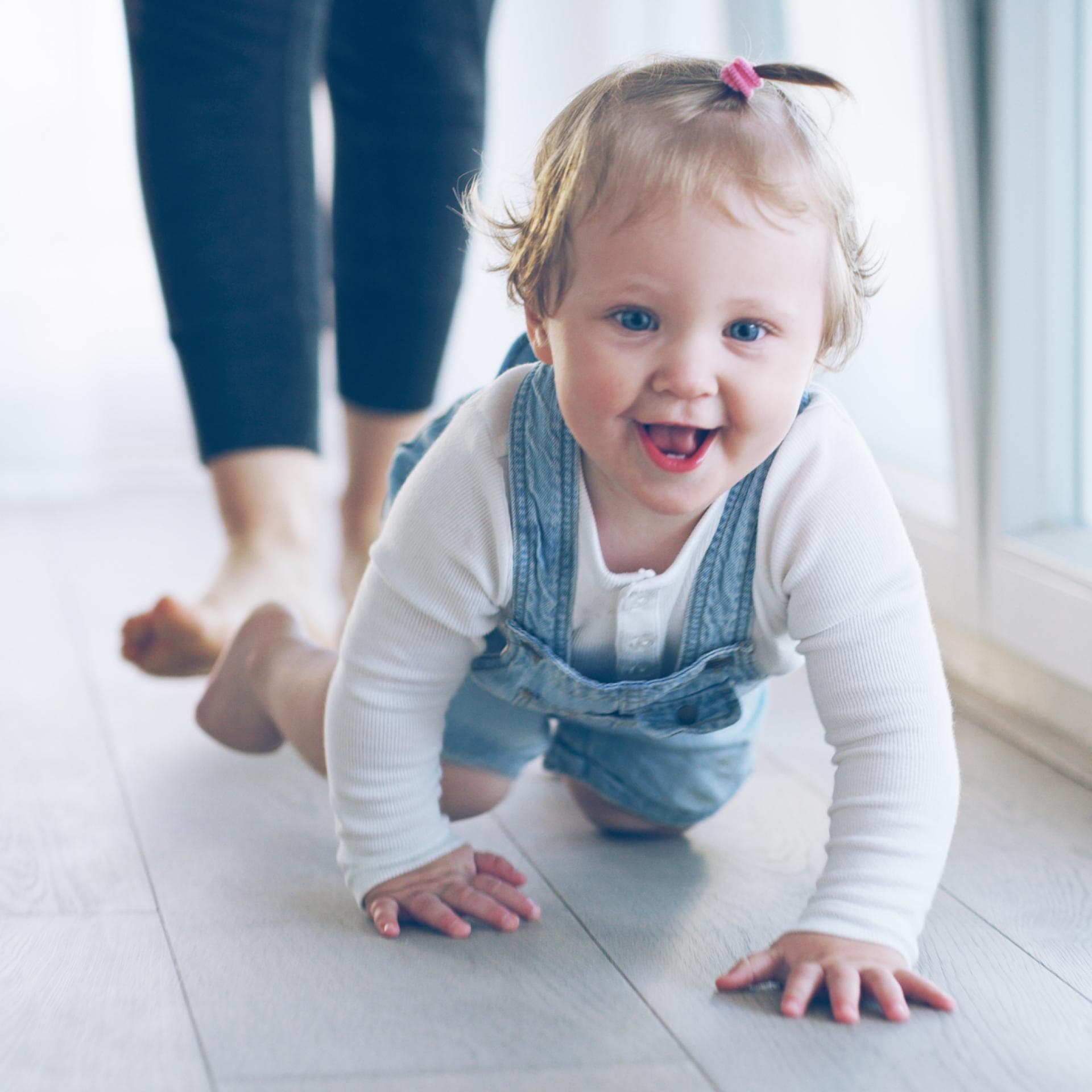 Kleines Mädchen krabbelt grinsend über den Fußboden.