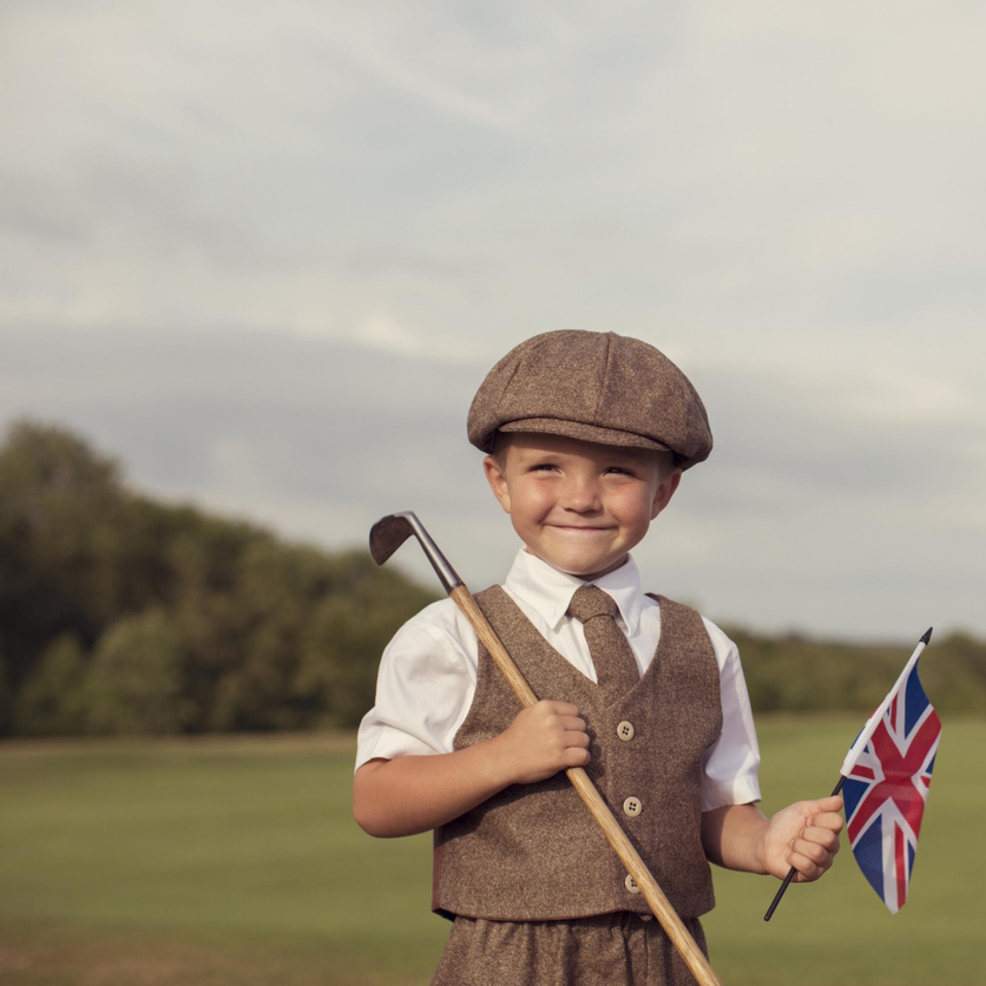 Englischer kleiner Junge in Vintage-Kleidung hält eine britische Flagge in der Hand