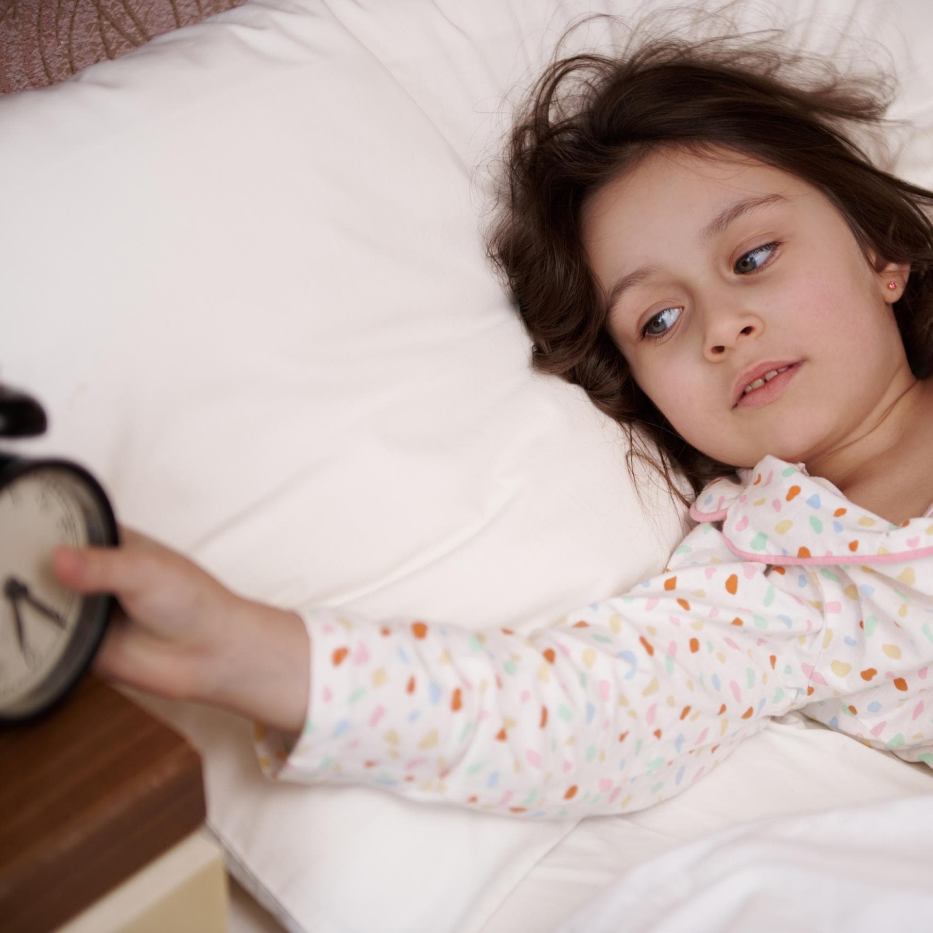 Mädchen liegt im Bett und stellt ihren Wecker aus.