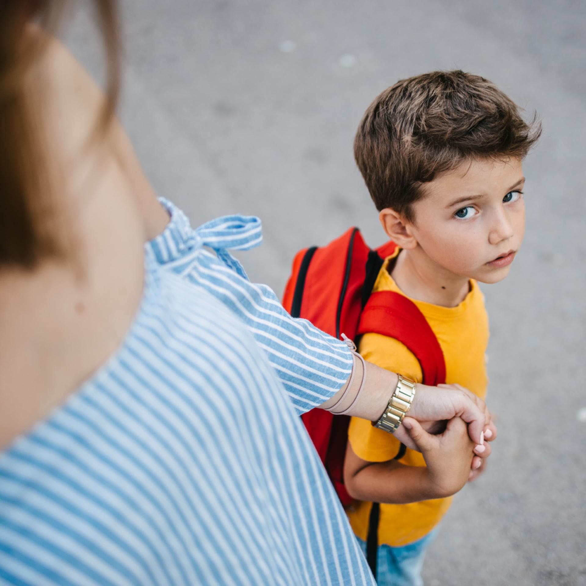 Mutter hält die Hand ihres Sohnes und bringt ihn zur Schule.