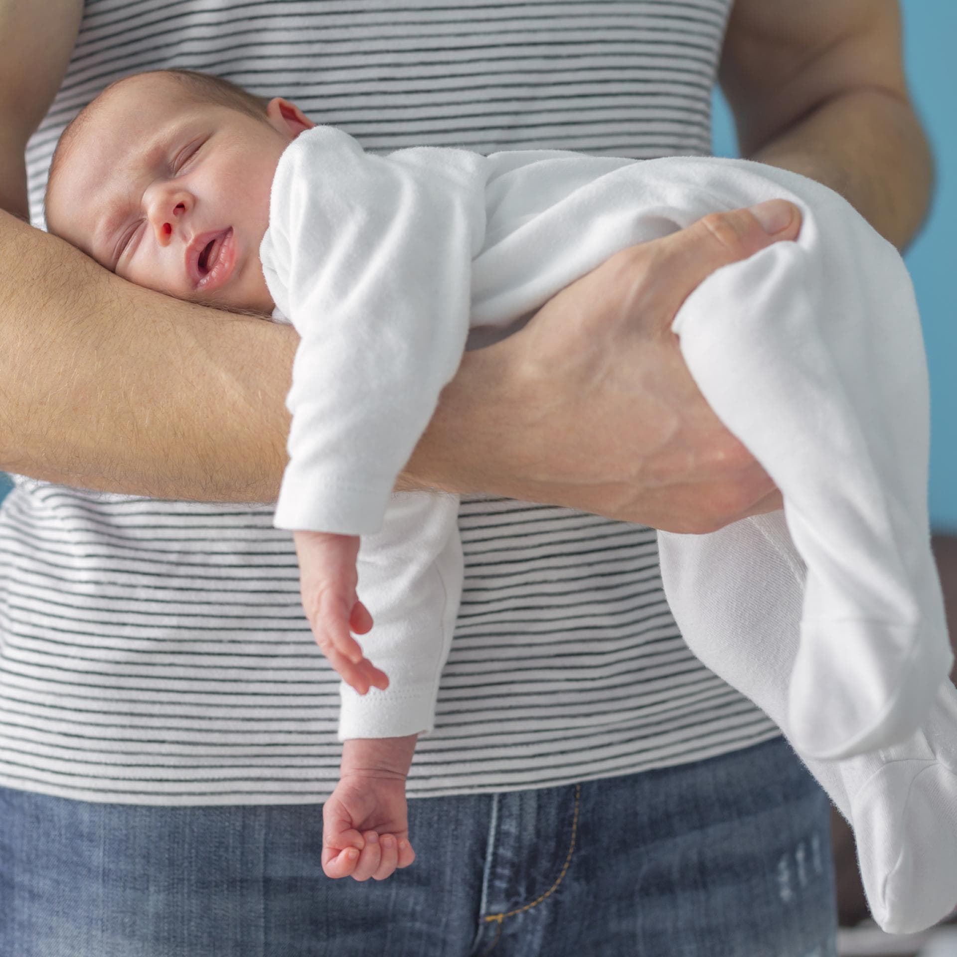 Ein Vater hält sein Neugeborenes im Fliegergriff vor seinem Bauch
