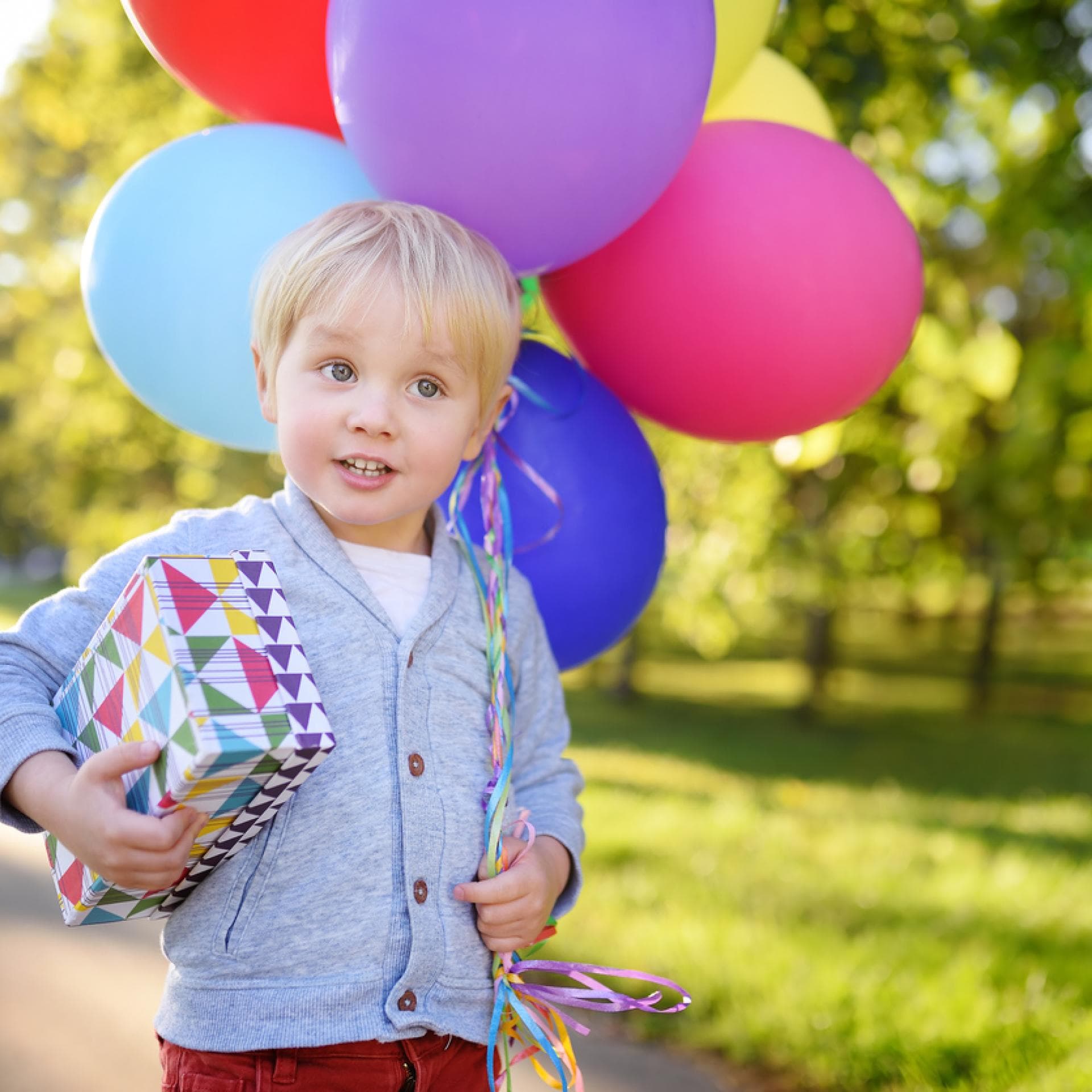 Kleiner blonder Junge feiert 3 Geburtstag und trägt Ballon und Geschenk. 