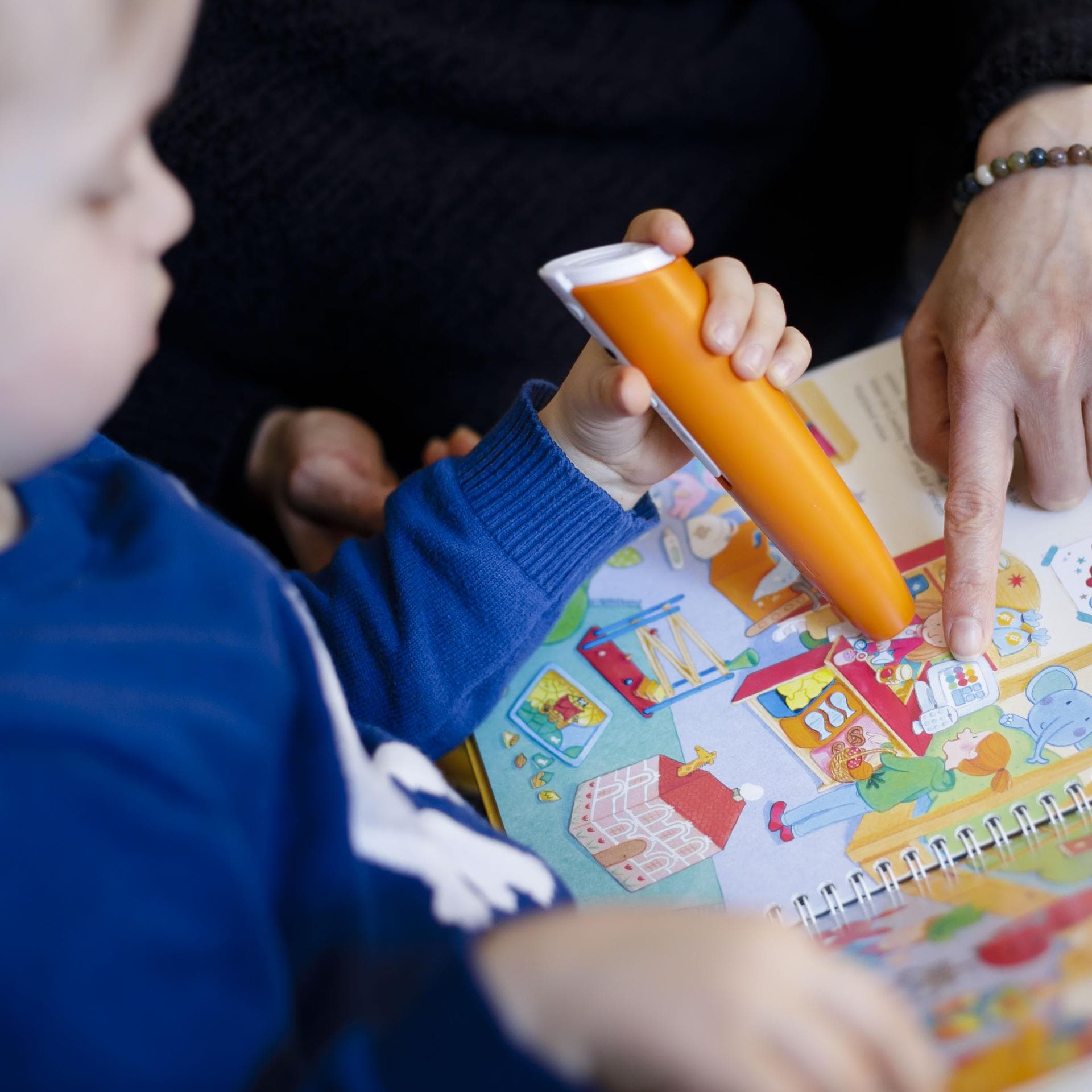 Ein kleiner Junge schaut gemeinsam mit einer Frau ein Tiptoi-Kinderbuch an.