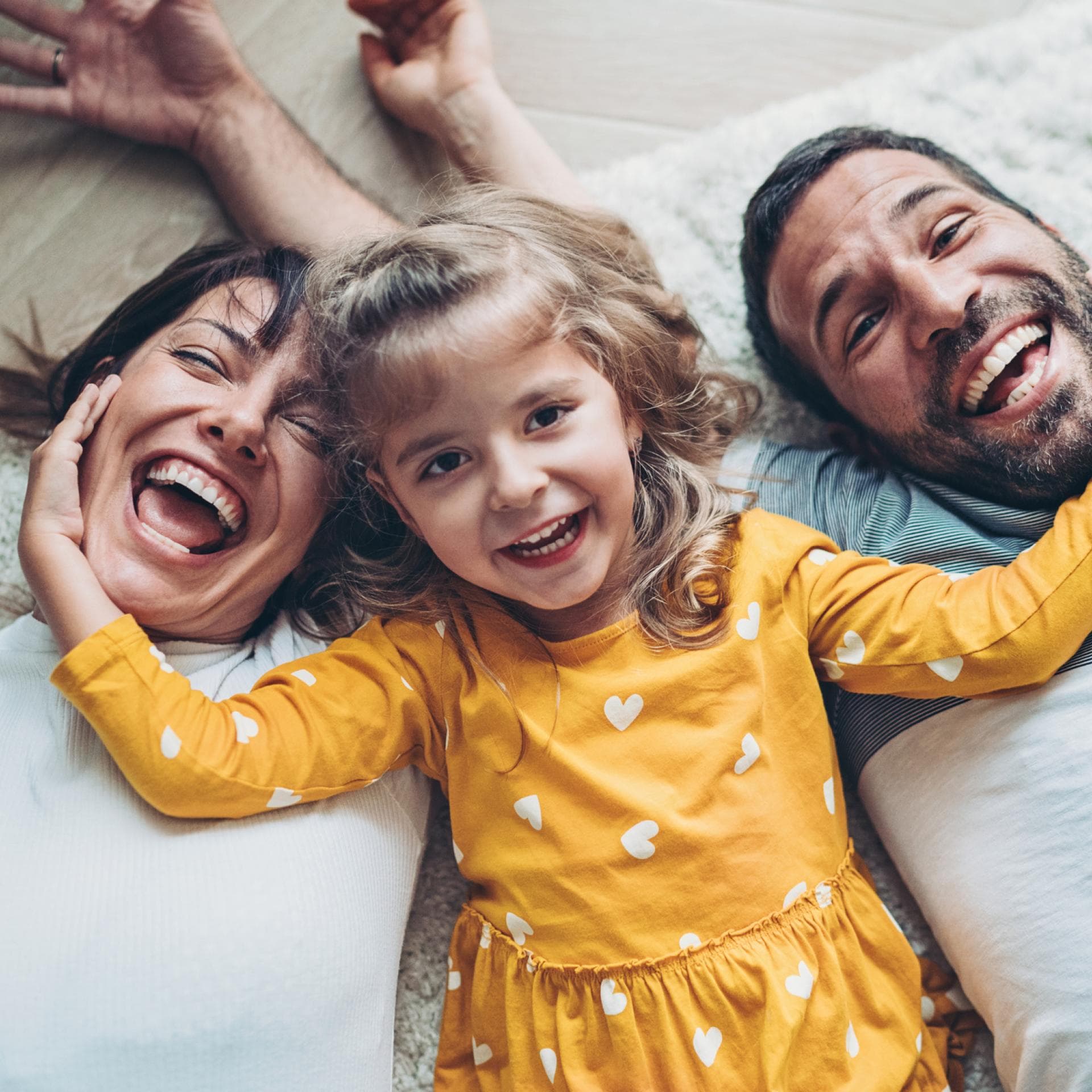 Lachende Eltern liegen mit ihrem Kind auf dem Boden.