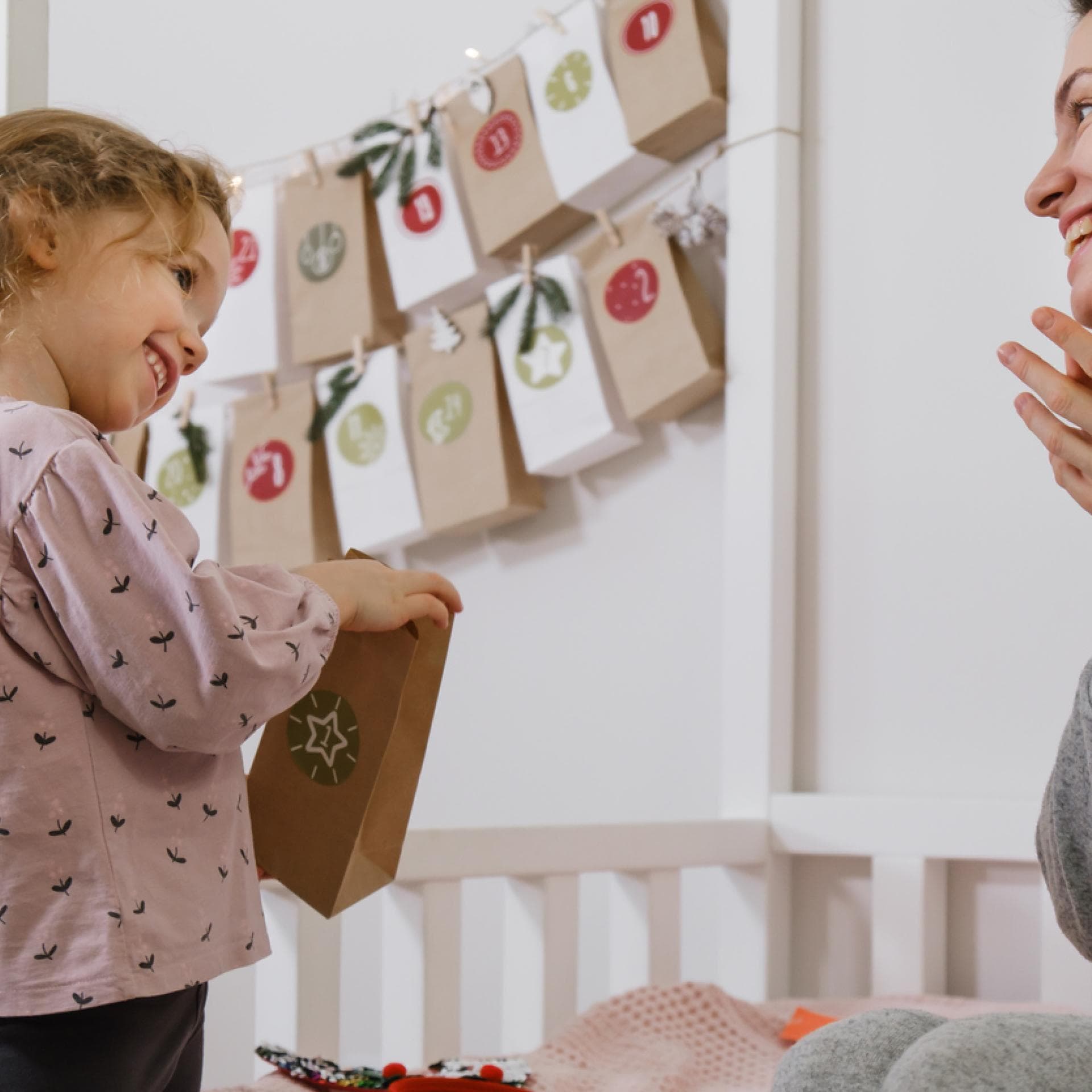 Kleines Mädchen öffnet ihren Montessori-Adventskalender. Und Mama freut sich mit!