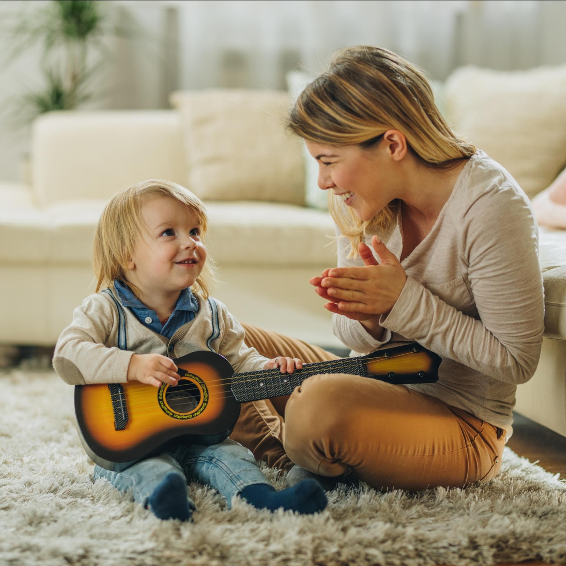 Eine Mama applaudiert ihrem kleinen Sohn, weil er Gitarre spielt