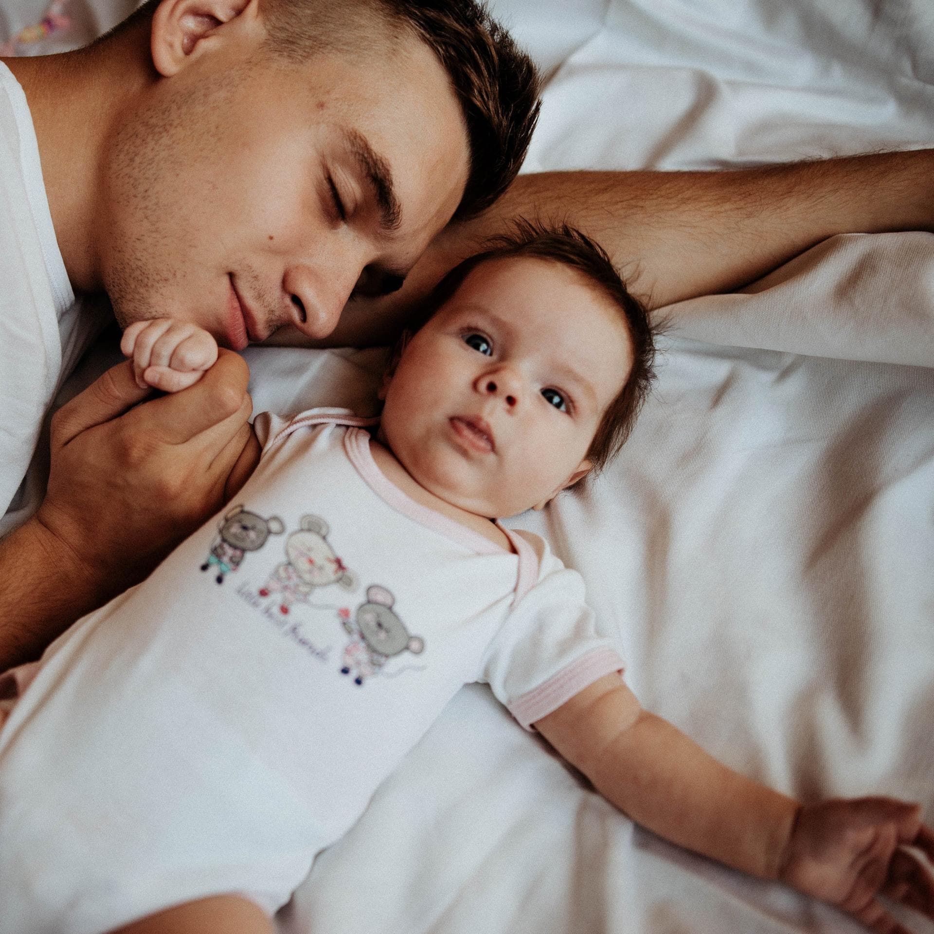 Papa hält beim Schlafen die Hand seines Babys. 