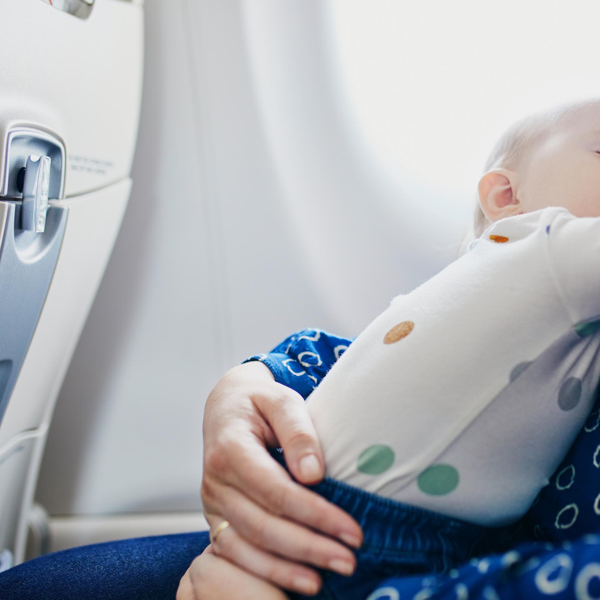 Ein kleines Baby schläft im Flugzeug auf dem Schoß seiner Mutter. 