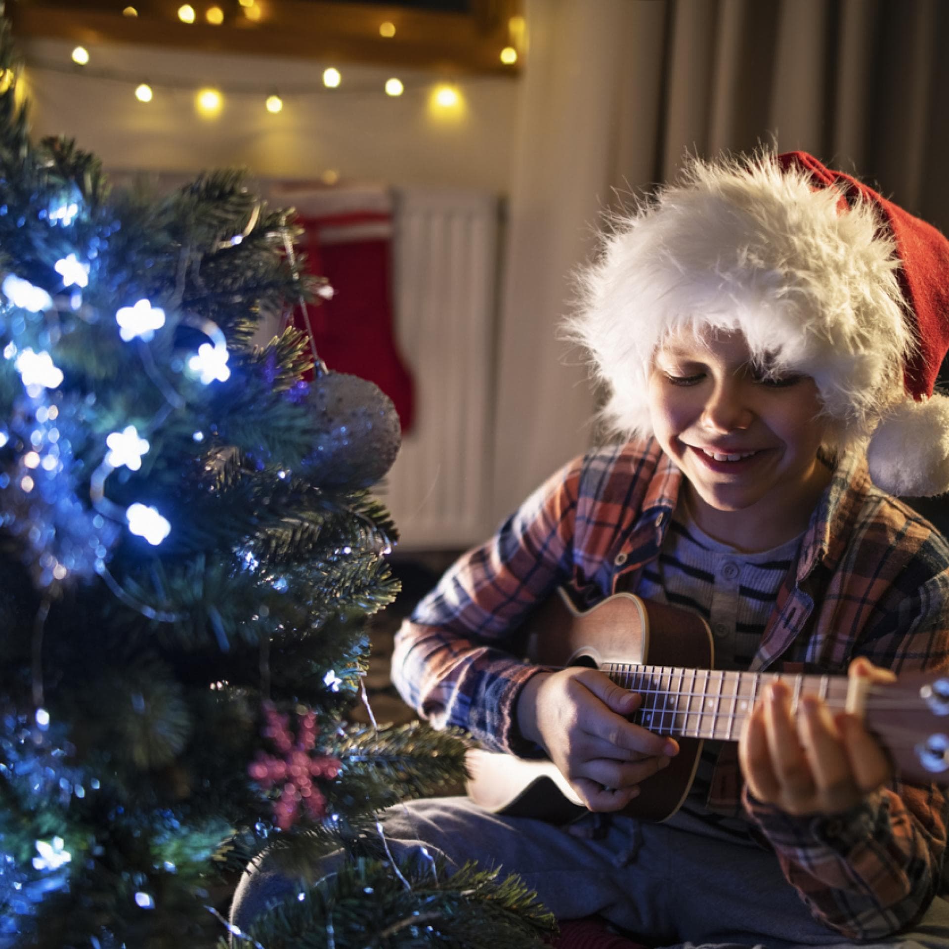 Junge spielt Gitarre und singt ein Weihnachtslied für Kinder unterm Tannenbaum.