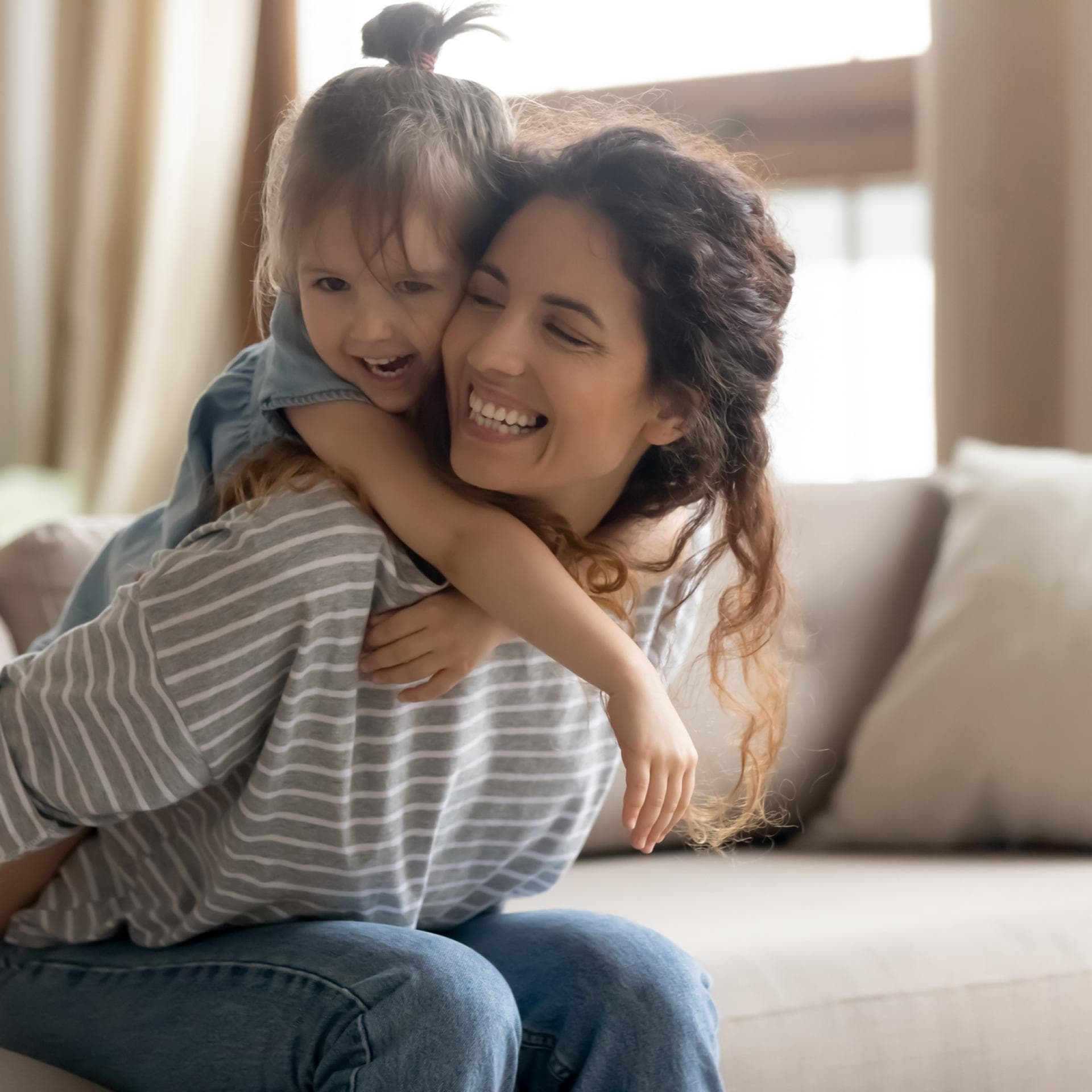 Mutter trägt ihr Kind auf dem Sofa sitzend huckepack.