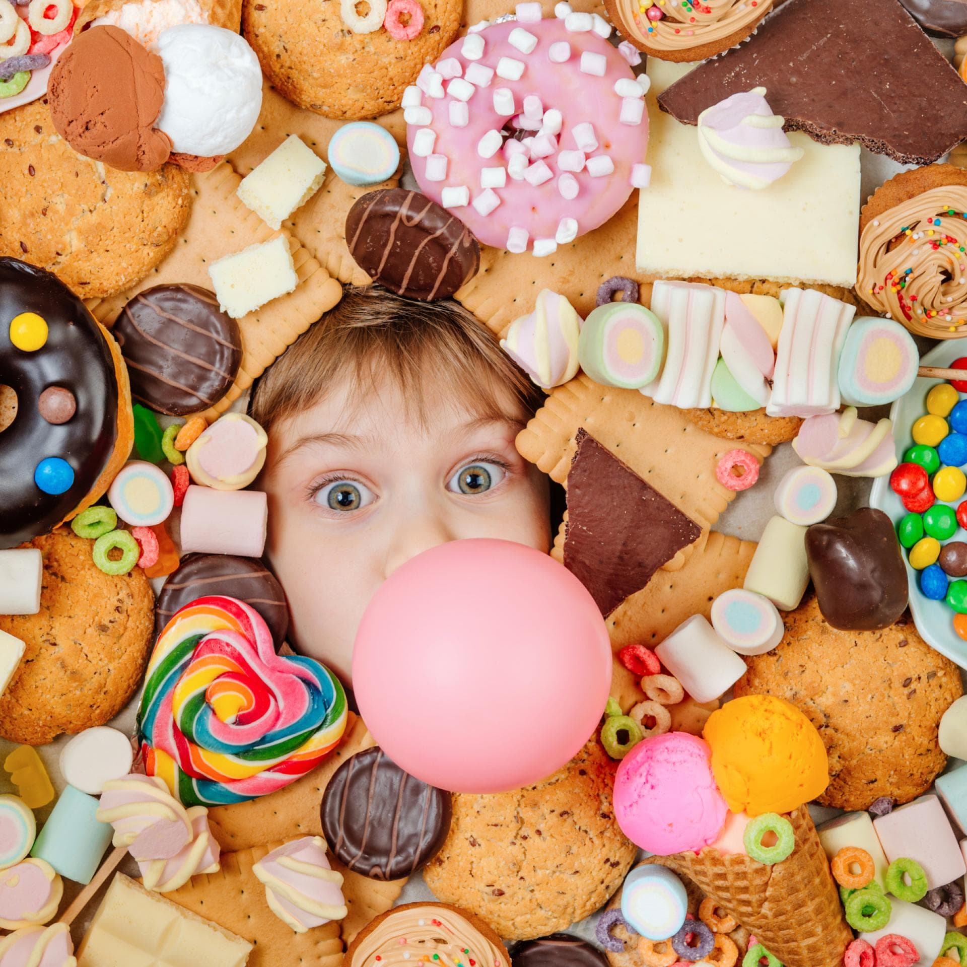 Kleines Kind, das unter vielen süßen Speisen liegt.