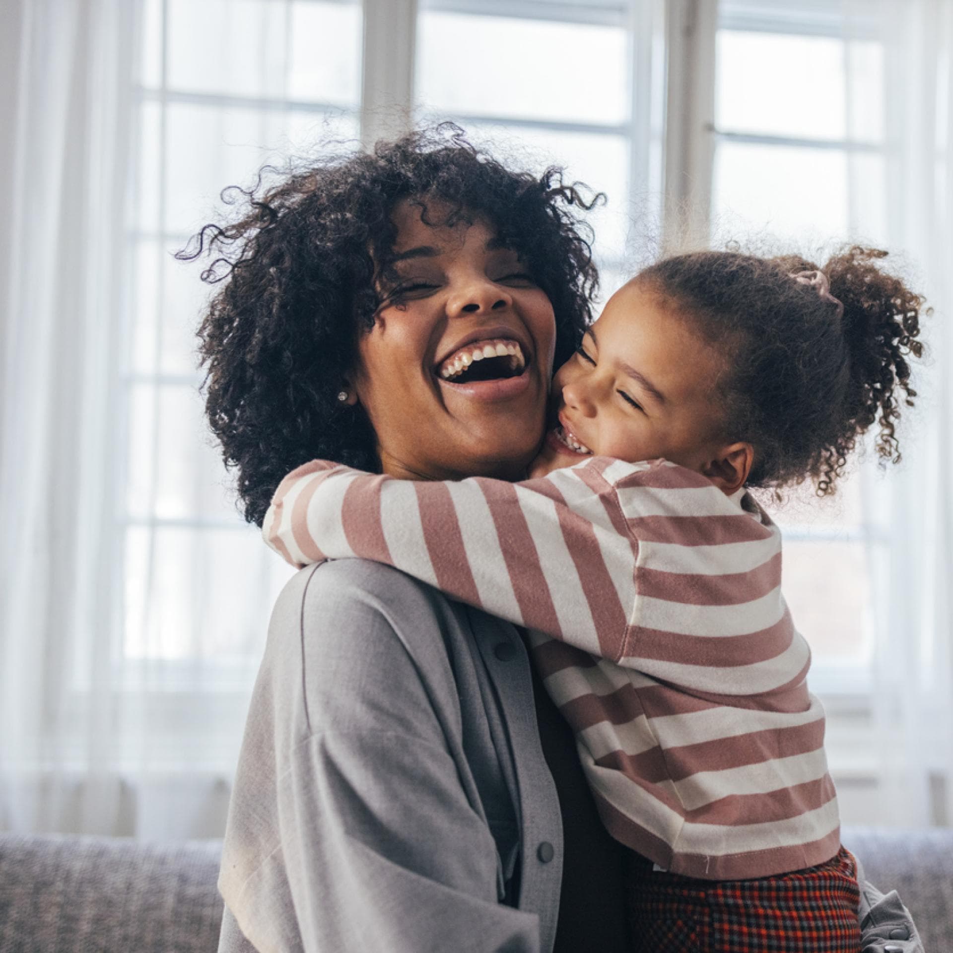 Lachende Mutter wird von ihrer Tochter umarmt.