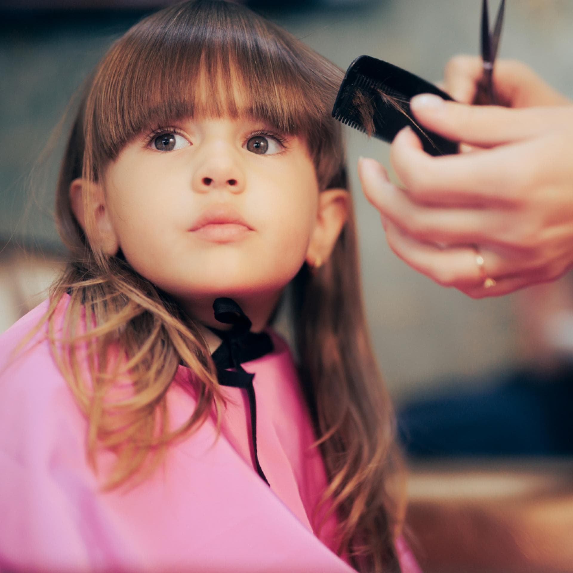 Einem kleinen Mädchen mit langen haaren wird der Pony geschnitten.