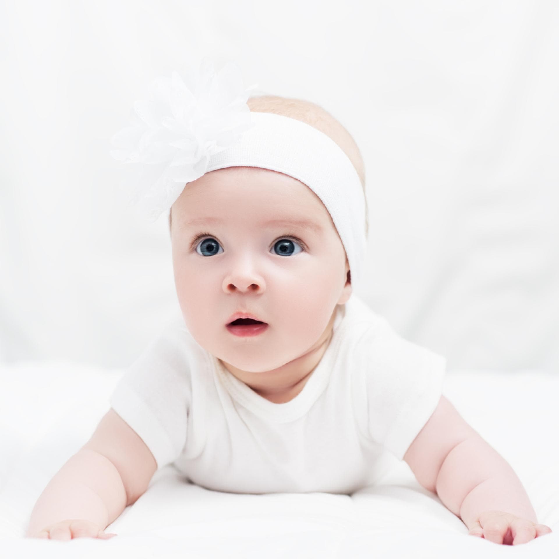 Baby in Bauchlage mit niedlichem Kopfband.