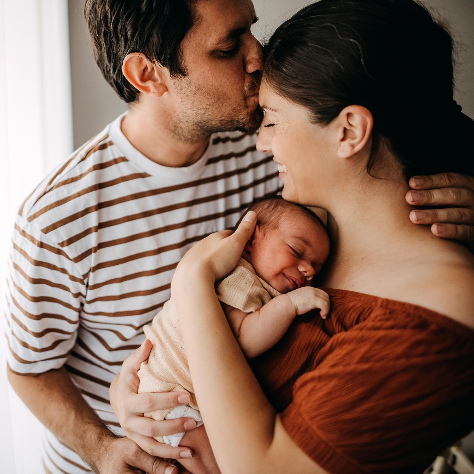 Paar mit Baby im Arm küsst sich.