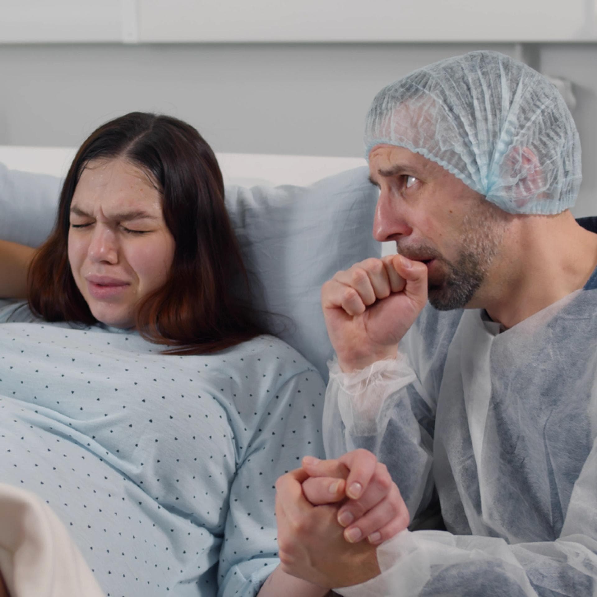 Verängstigter Ehemann, der im Kreißsaal die Hand einer Frau hält