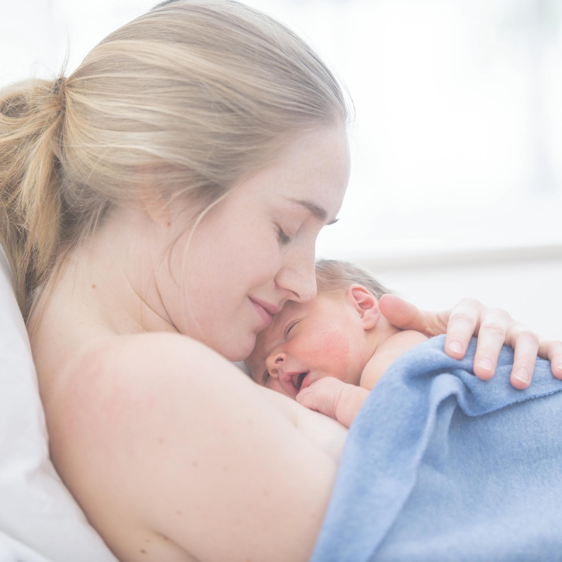 Frau liegt mit Baby auch der Brust im Wochenbett.