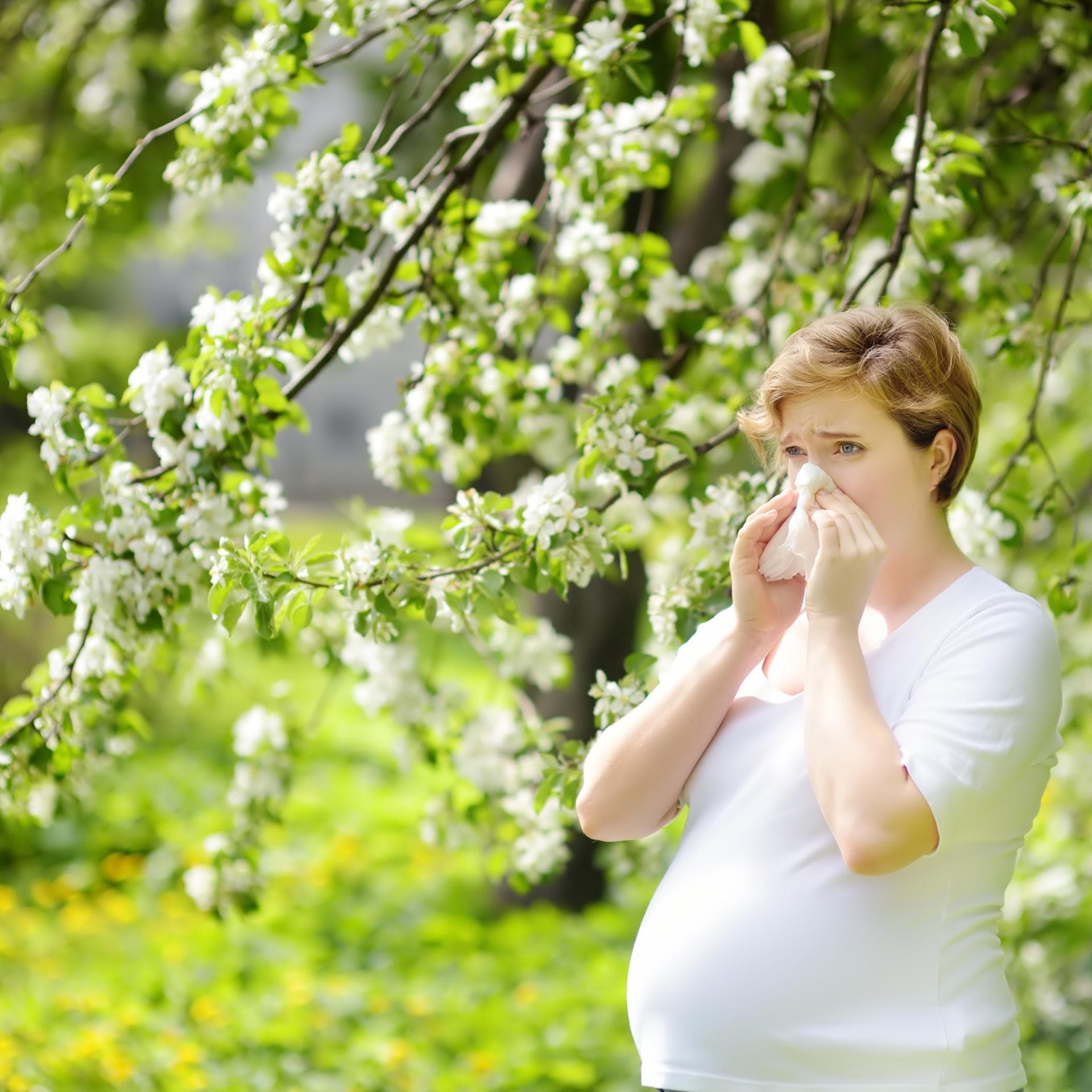Eine schwangere Frau putzt sich auf einer Wiese die Nase. 