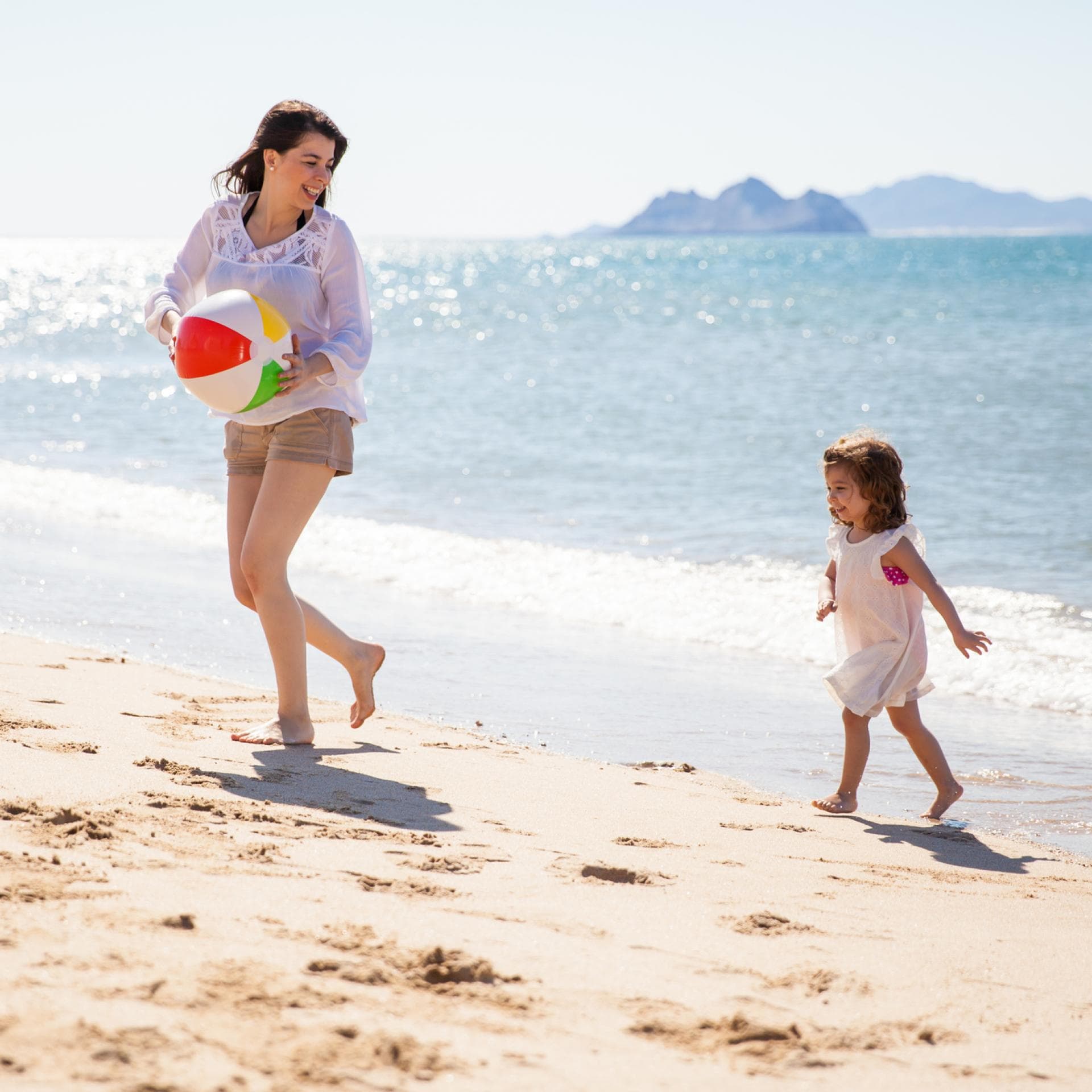 Junge Frau spielt mit Kind am Strand.