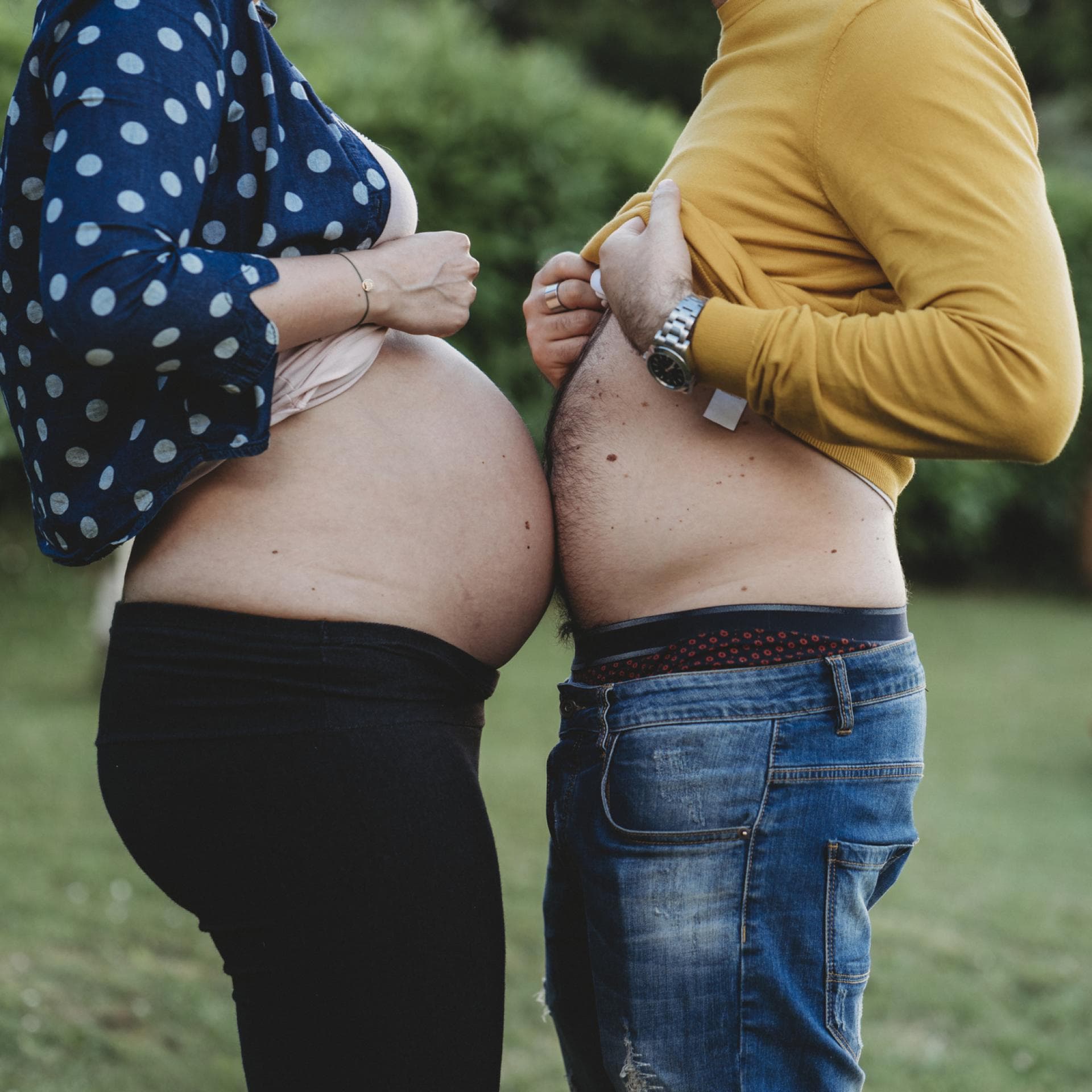 Schwangere Frau und ihr Mann halten ihre Bäuche aneinander.