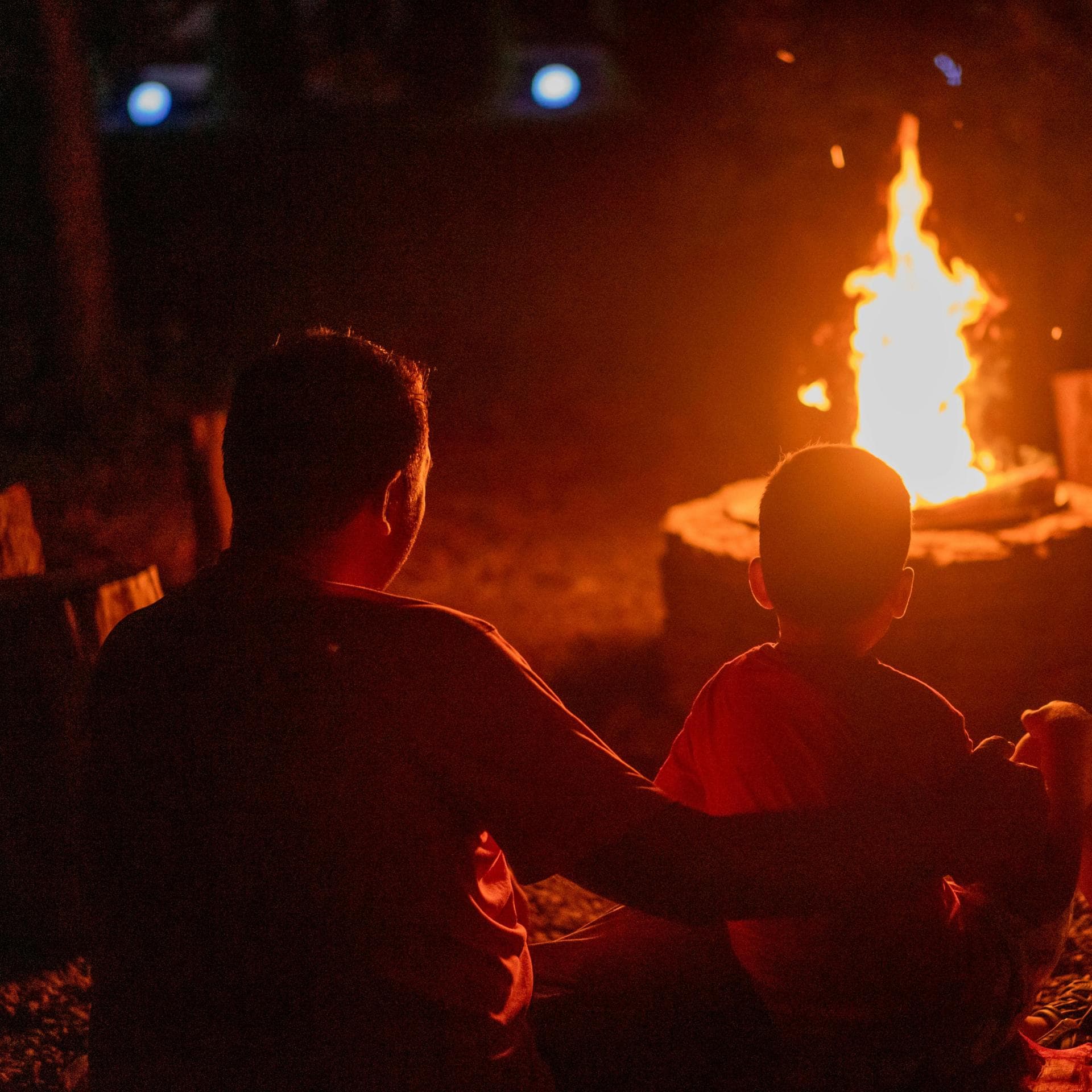 Ein Vater sitzt mit seinen beiden Kindern am Lagerfeuer. 
