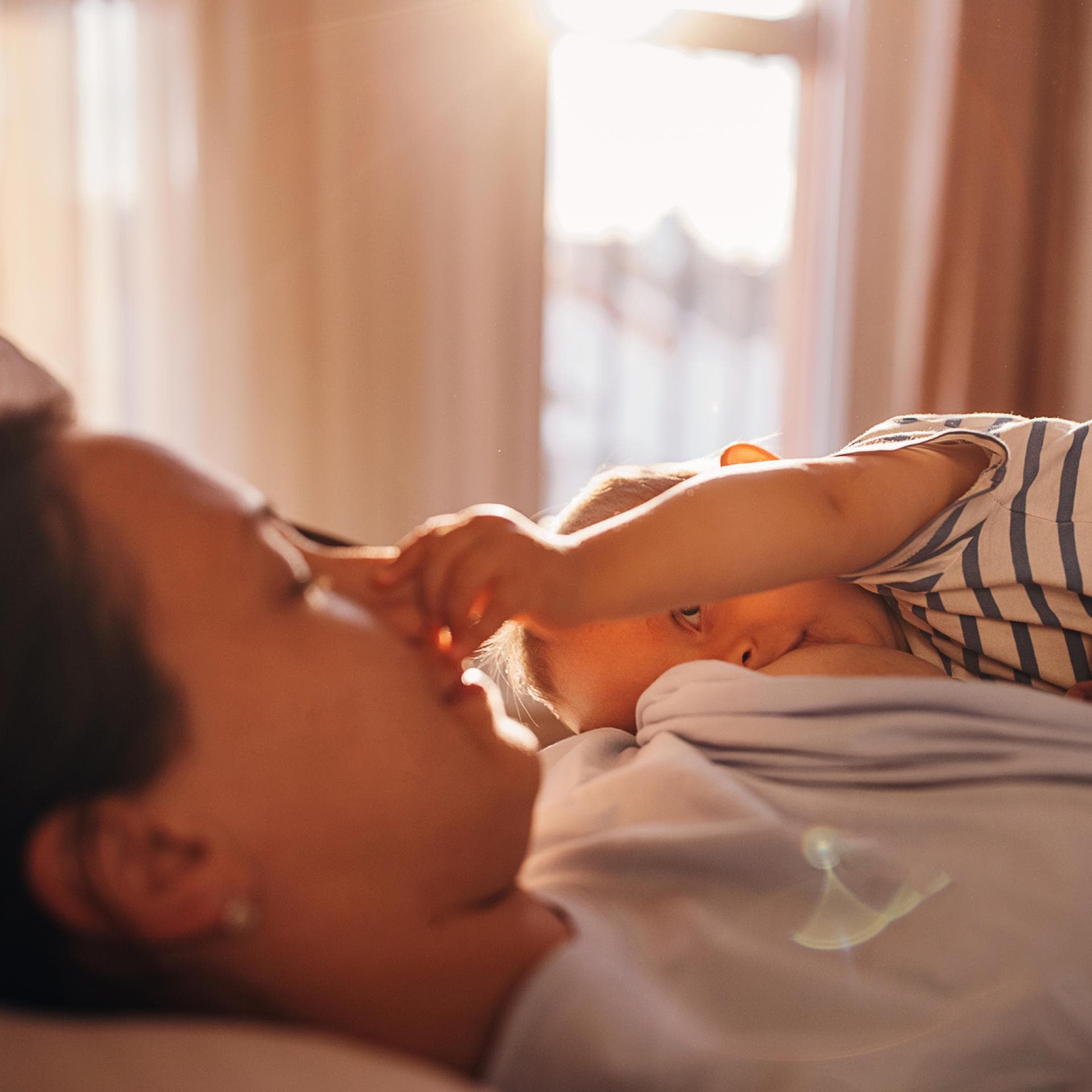 Ein Baby wird gestillt und fummelt dabei an Mamas Nase.
