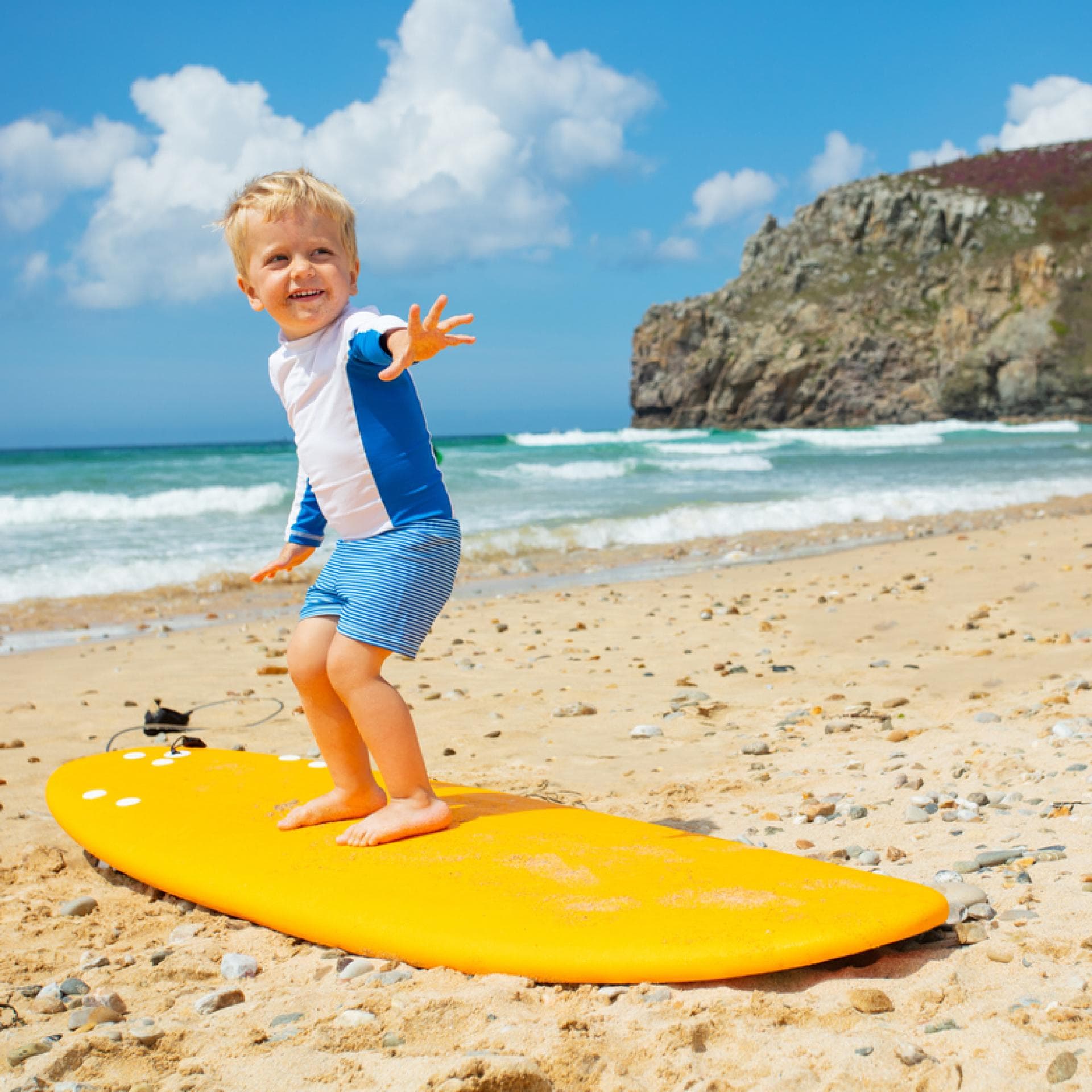 Kleiner Junge steht auf einem Surf-Brett.
