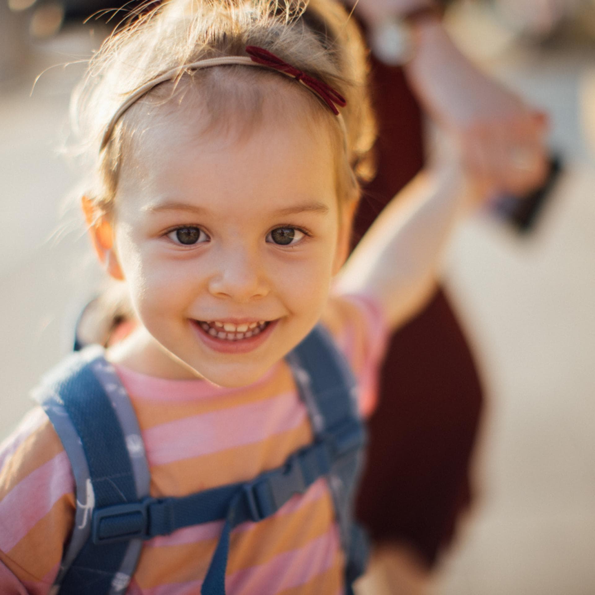 Mädchen mit Kita-Rucksack an der Hand ihrer Mama