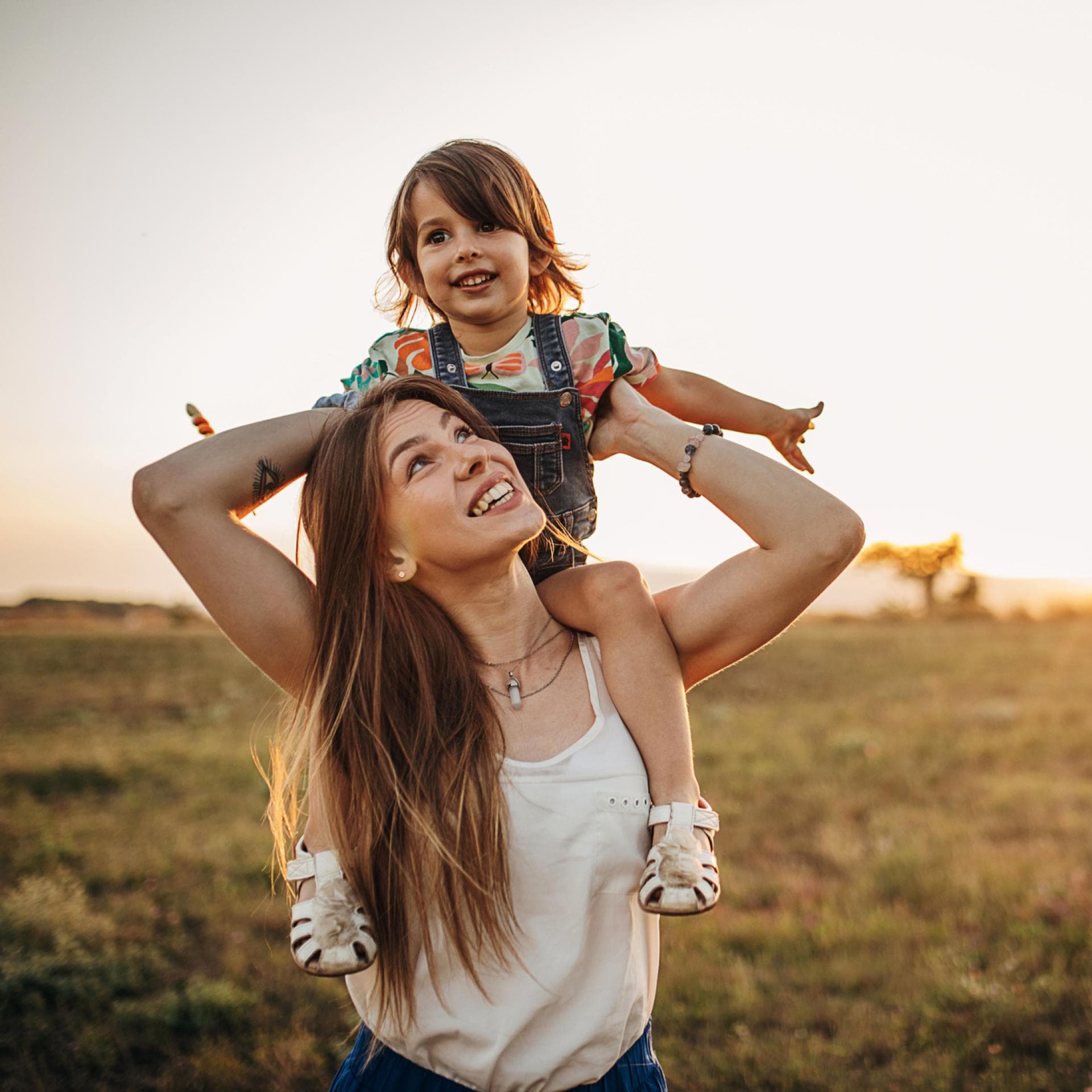 Mutter trägt Kind auf einer Wiese auf den Schultern.