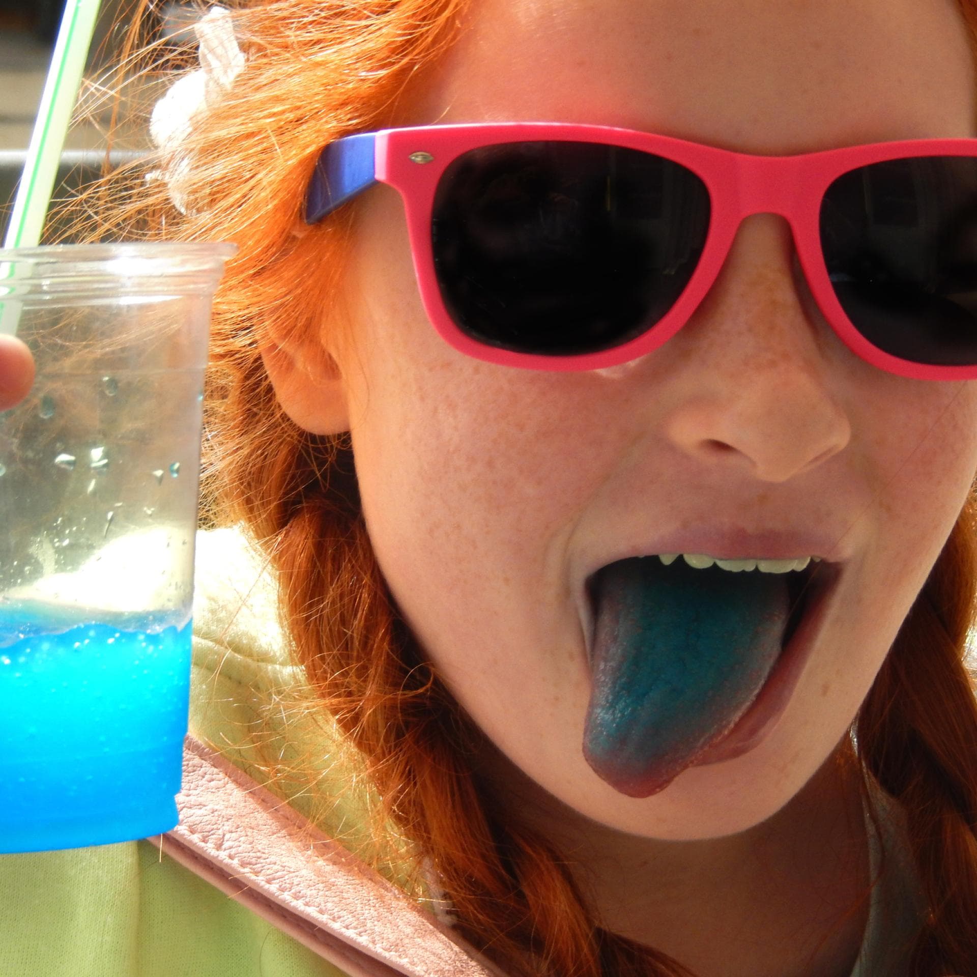 Mädchen streckt blaue Zunge heraus und hält Slushie in der Hand.