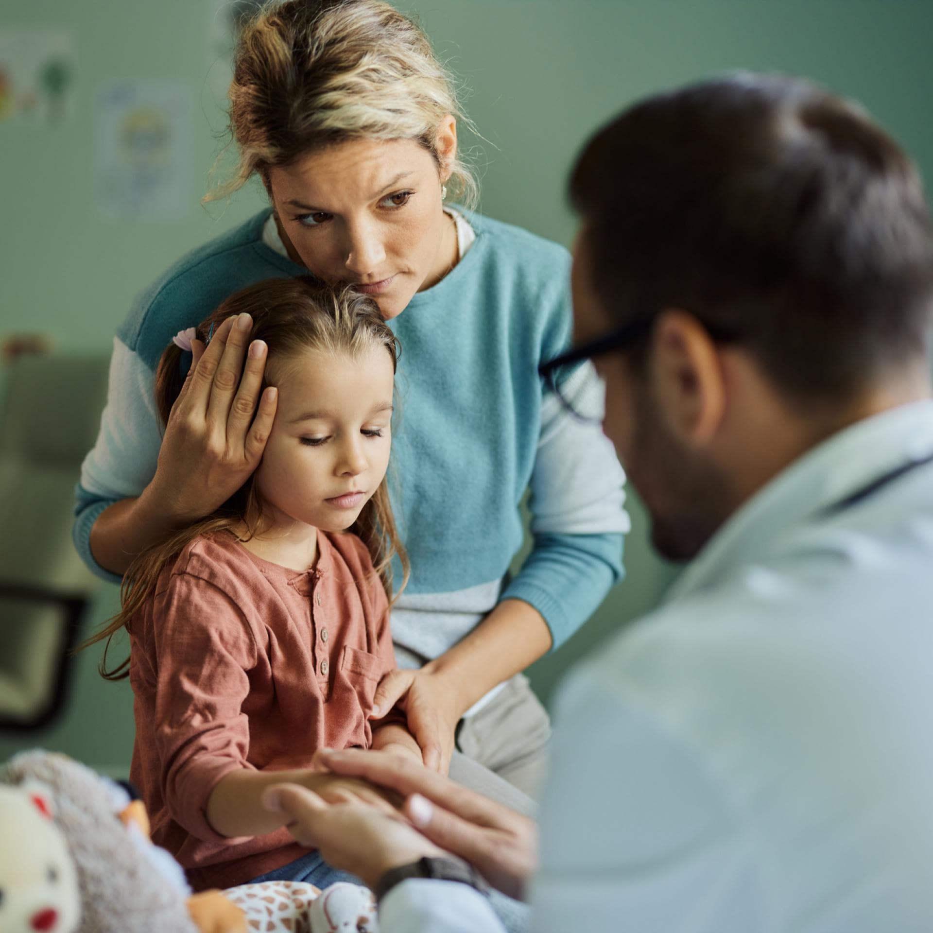 Eine Mutter und ein Vater trösten ihre kranke Tochter.