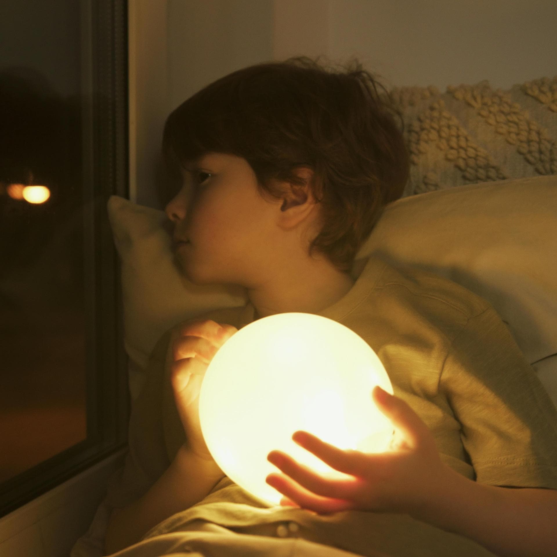 Ein Kind, das beim Einschlafen traurig aus dem Fenster guckt