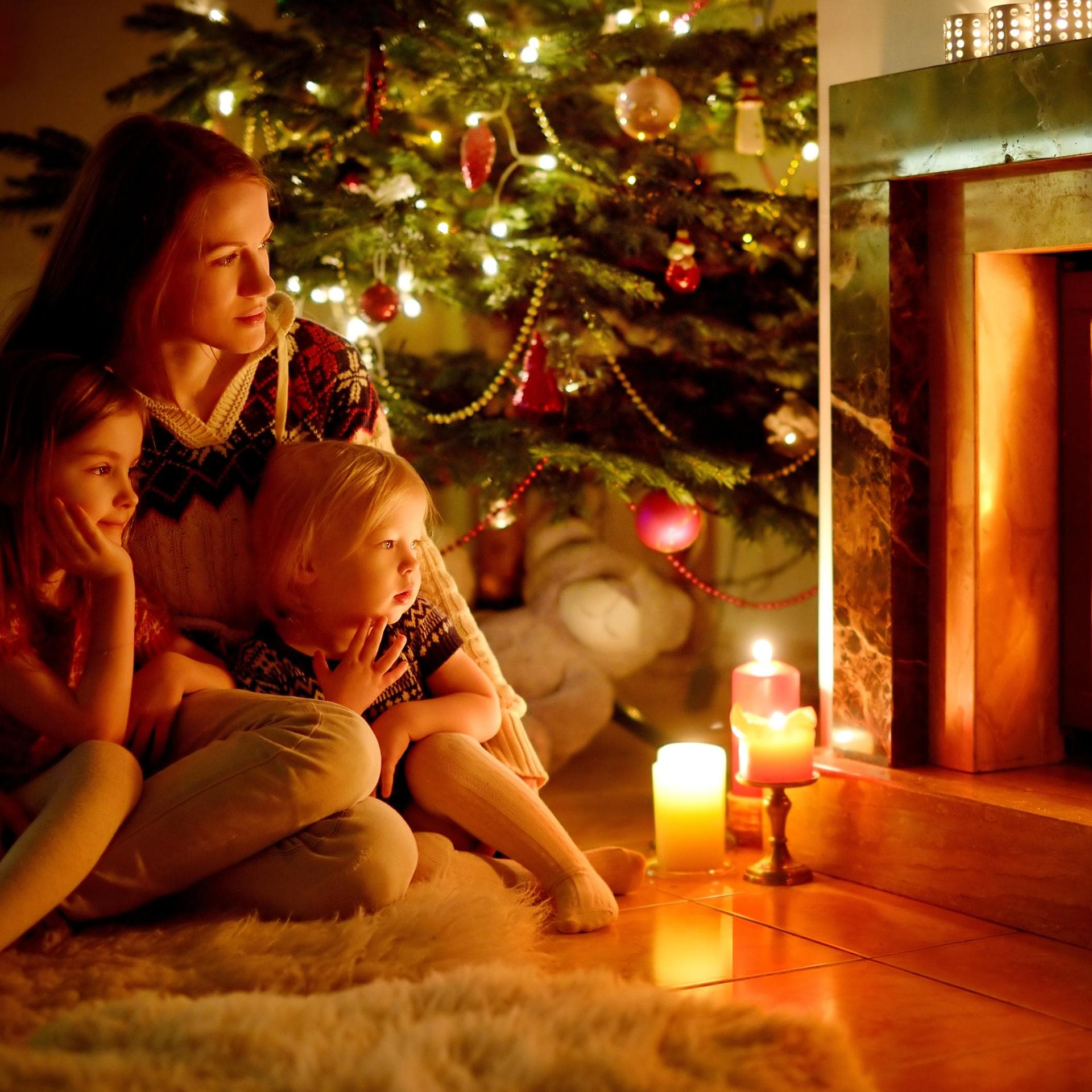 Mutter sitzt mit ihren Kindern am Kamin.