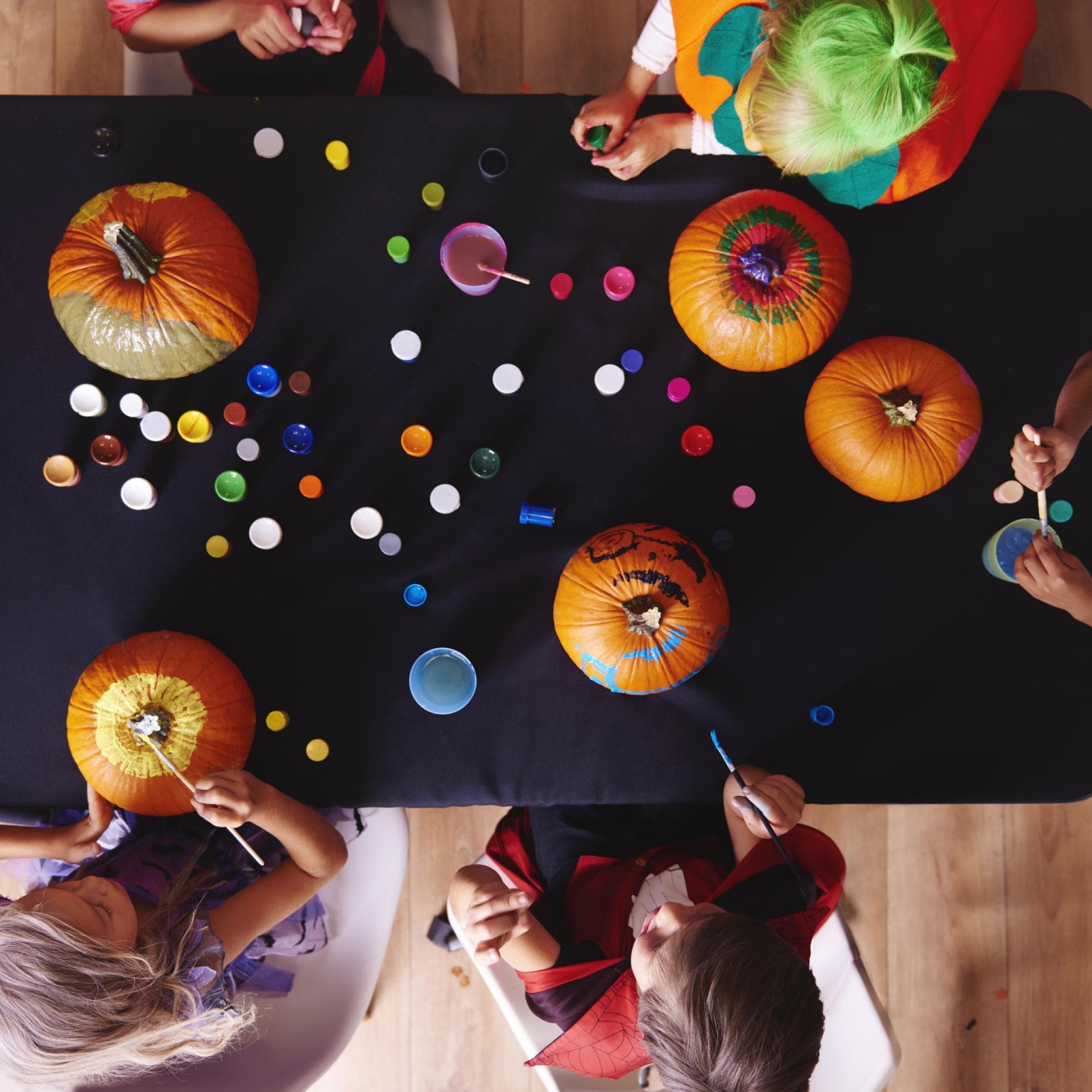 Kinder sitzen am Tisch und bemalen Kürbisse.