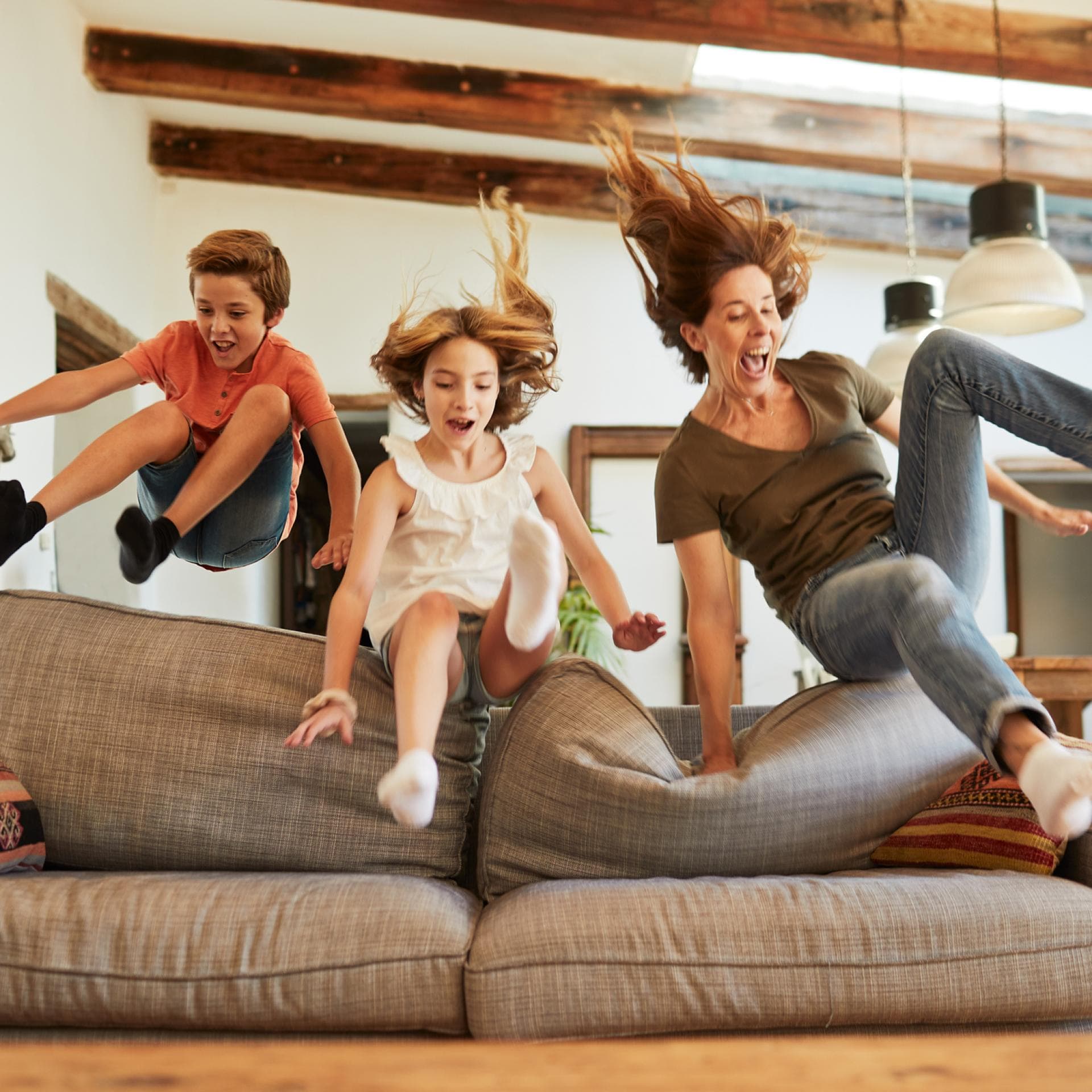 Mutter und zwei Kinder springen zusammen aufs Sofa